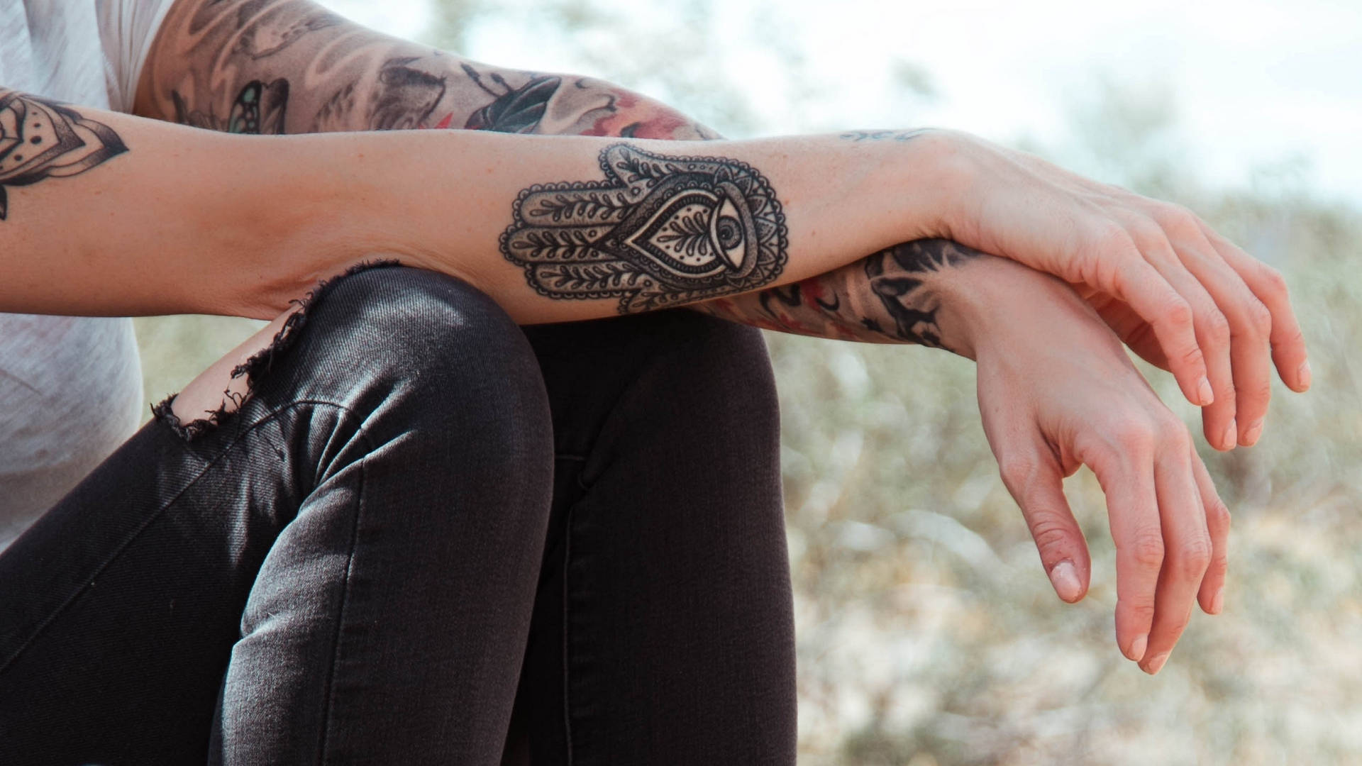 Tattoo 桌布 壁紙 — 特寫紋身手臂放在膝蓋上，帶有複雜的Hamsa手設計，中心有一隻眼睛。