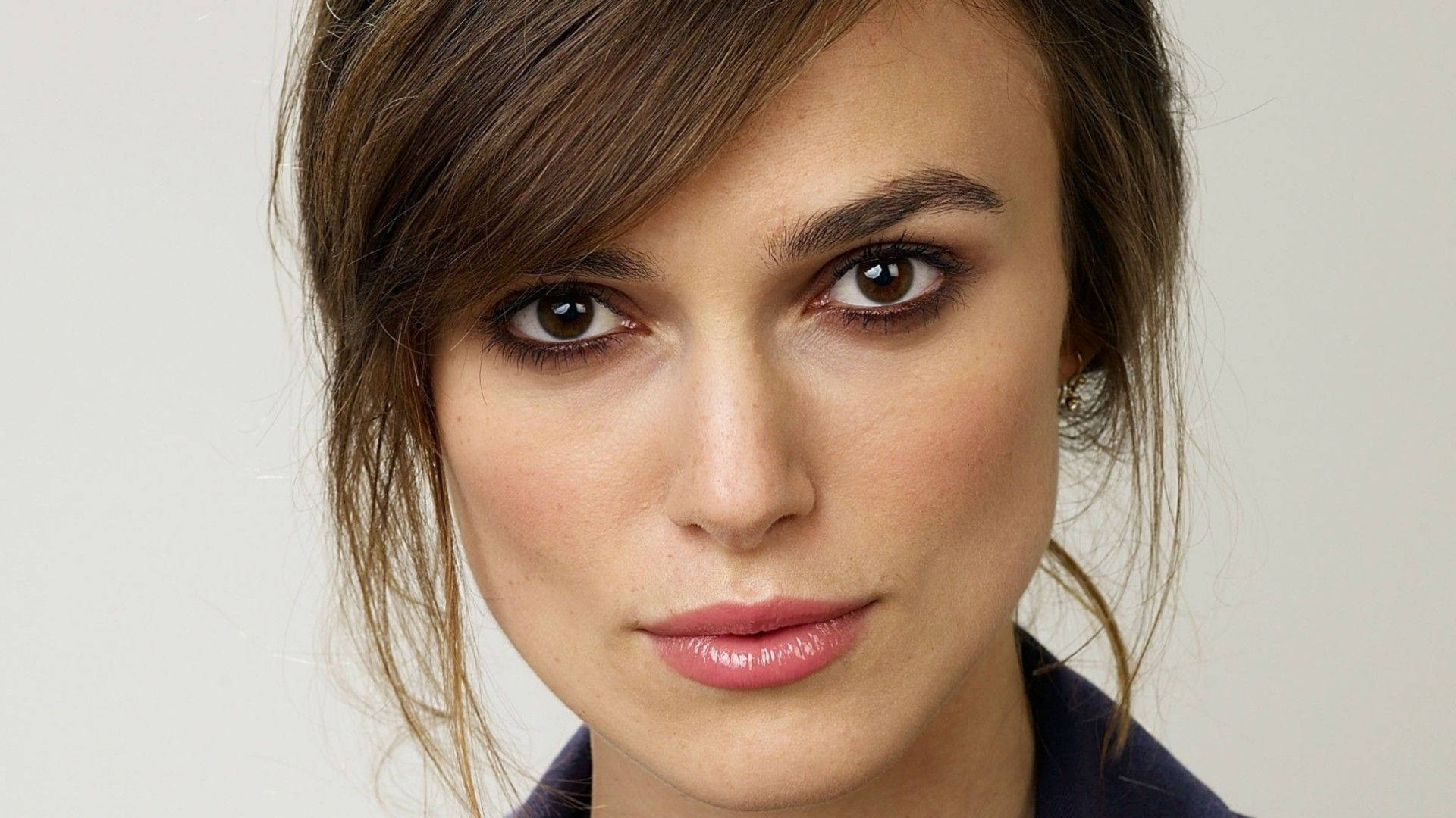 Keira Knightley 桌布 壁紙 — 特寫肖像，一位擁有棕色眼睛和柔和妝容的女性，背景為純色淺色。