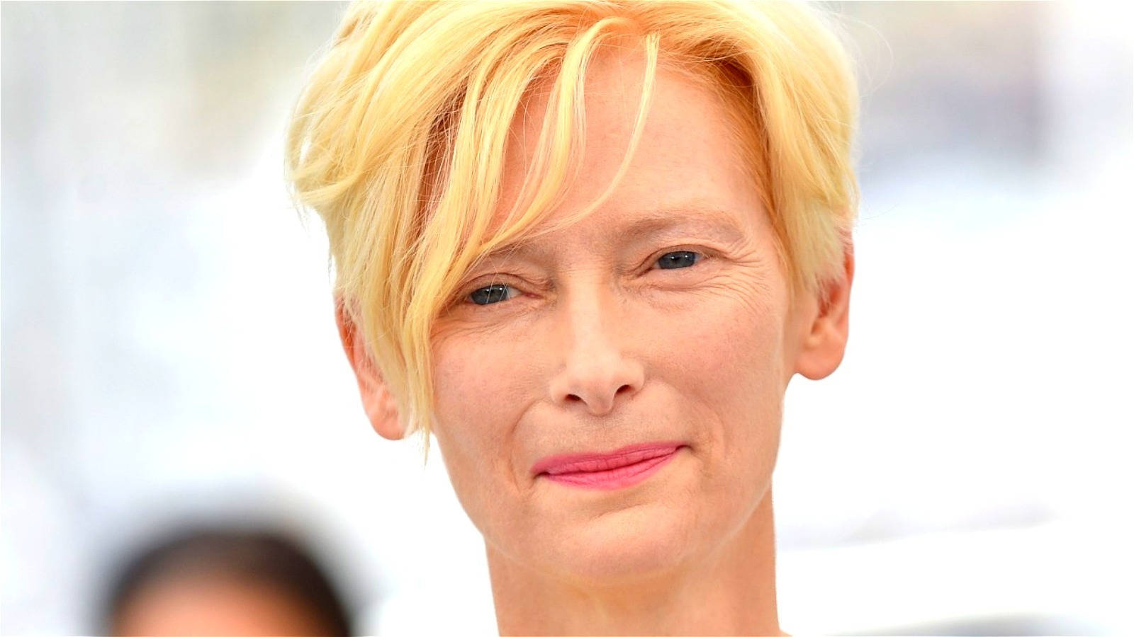 Celebrity 桌布 壁紙 — 特寫肖像，一位短金髮、塗粉紅色唇膏的女性，在明亮模糊的背景前溫柔微笑。