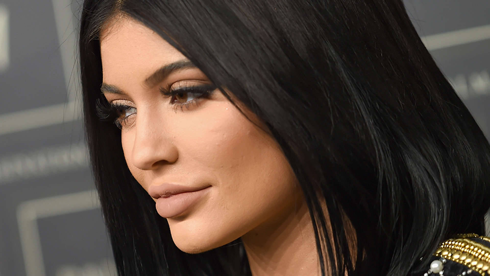 Kylie 桌布 壁紙 — 特寫肖像，一位長黑髮、煙燻眼妝的女性在活動中低頭向下看。