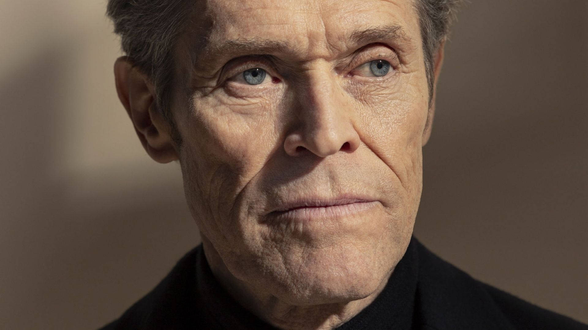 Willem Dafoe 桌布 壁紙 — 特寫肖像，一個飽經風霜的男人，擁有銳利的藍眼睛和深深的皺紋，背景是柔和的米色。