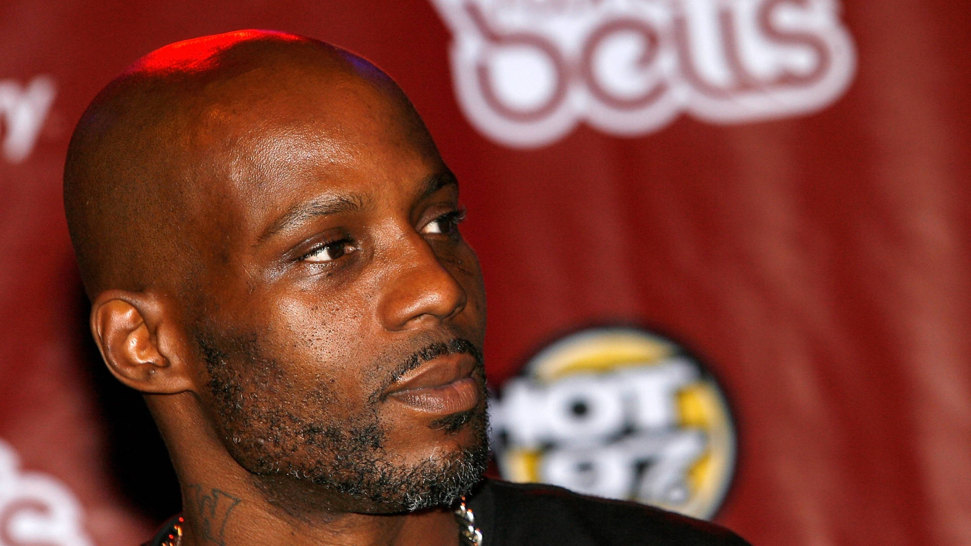 Dmx 桌布 壁紙 — 特寫肖像，一名光頭黑人男子留著山羊鬍，在帶有標誌的紅色背景前看向鏡頭外。
