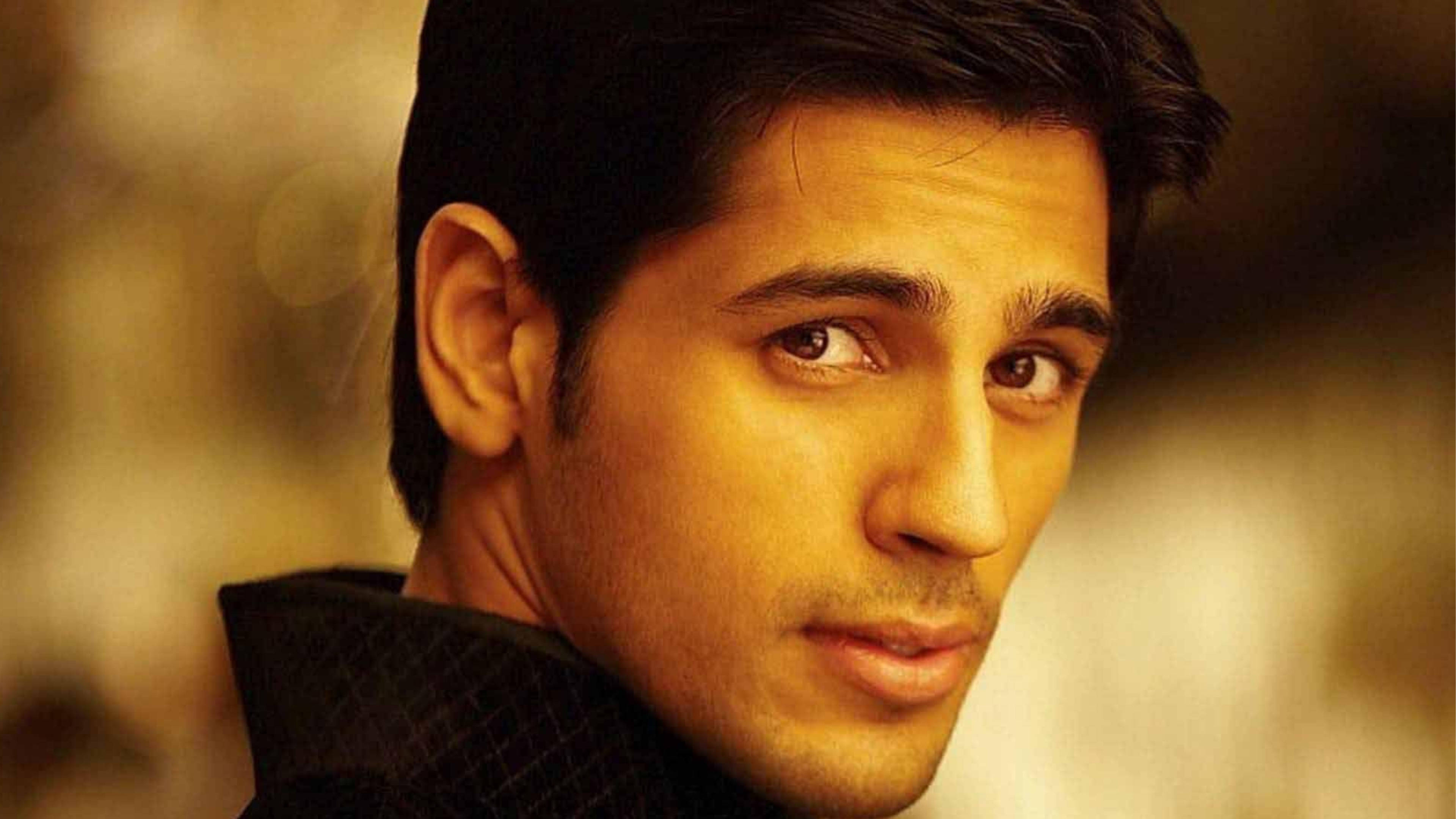 Sidharth Malhotra 桌布 壁紙 — 特寫肖像，一名深色頭髮、眼神銳利的男子，背景是溫暖的金色散景。