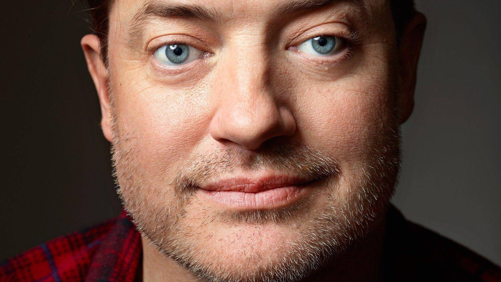 Celebrity 桌布 壁紙 — 特寫肖像，一名男子擁有引人注目的藍色眼睛和鬍渣，穿著紅色格紋襯衫，背景深色。