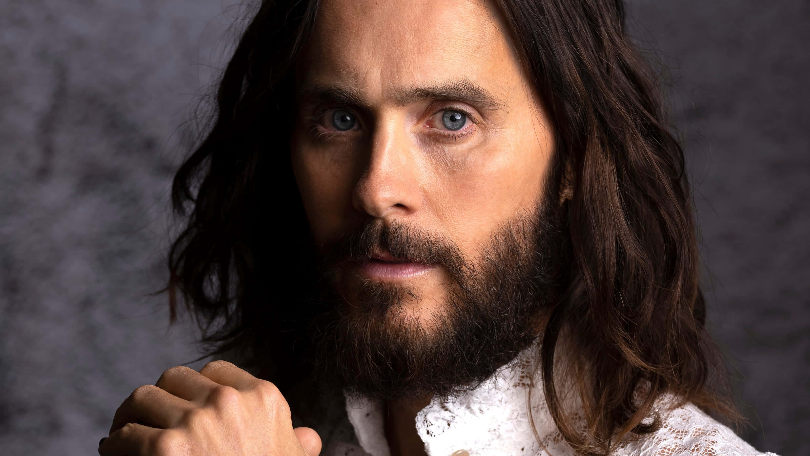 jared leto 桌布 壁紙 — 特寫肖像，一名留著長黑髮和鬍鬚的男子，穿著白色蕾絲襯衫，背景為有紋理的灰色。