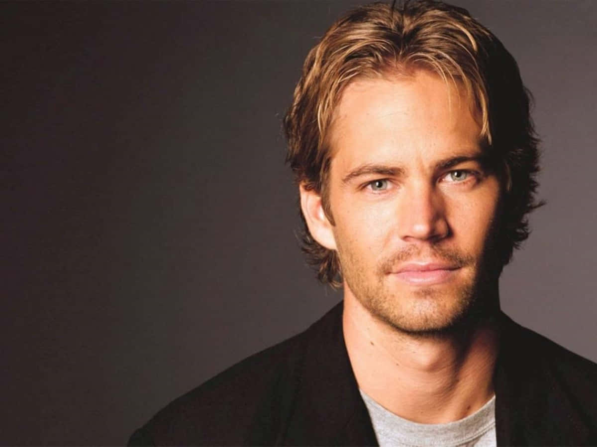Paul Walker 桌布 壁紙 — 特寫肖像，一名金髮綠眼的男子，身穿黑色外套內搭灰色襯衫，背景為深灰色。