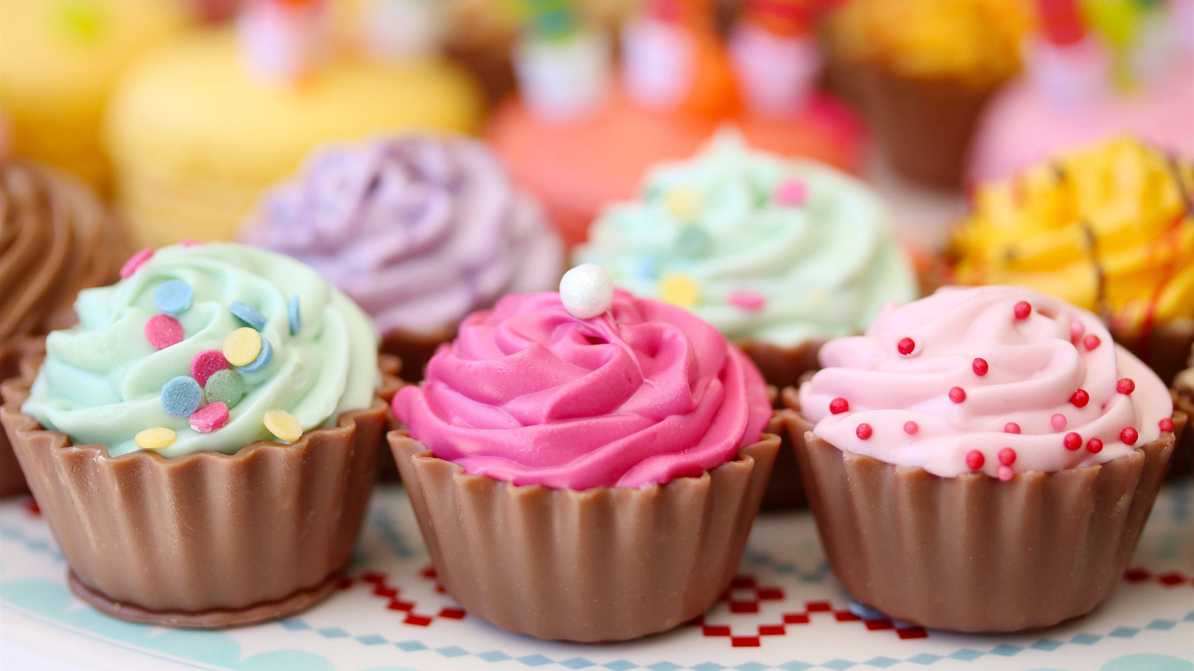 Cupcake 桌布 壁紙 — 特寫色彩繽紛的杯子蛋糕，上有漩渦狀糖霜和彩色糖粒，放在圖案碟子上。