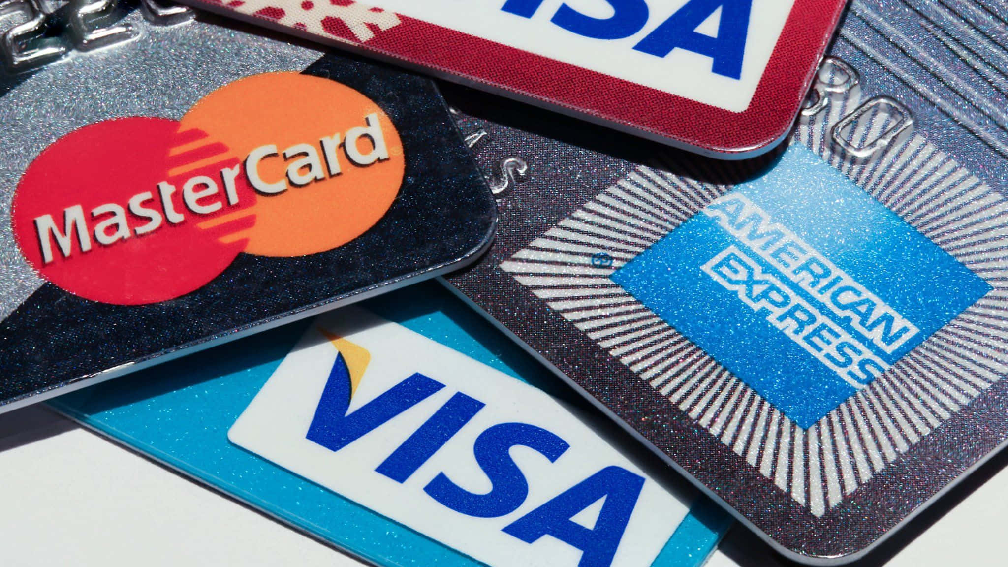 美國運通 桌布 壁紙 — 特寫重疊的信用卡，包括 MasterCard、Visa 和 American Express，在明亮光線下帶有閃亮表面。