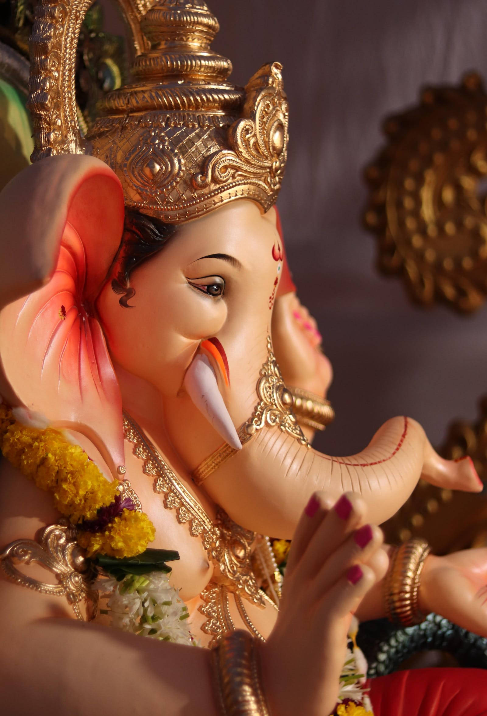 Ganesh 桌布 壁紙 — 特寫金色象神雕像，在溫暖陽光下飾有鮮花和珠寶。