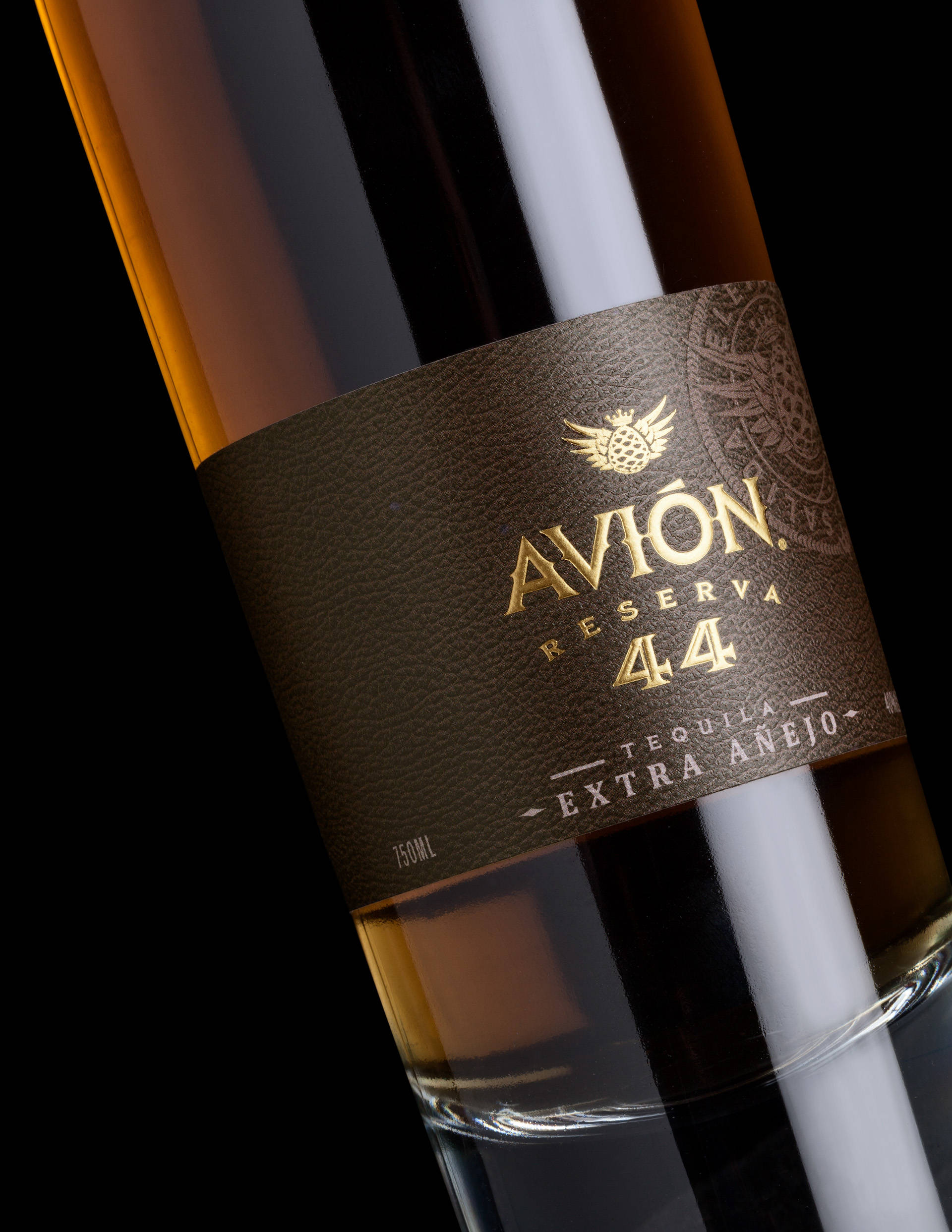 alcohol 桌布 壁紙 — 特寫鏡頭：Avion Reserva 44 龍舌蘭酒瓶，金色字體印在帶紋理的棕色標籤上，背景為黑色。