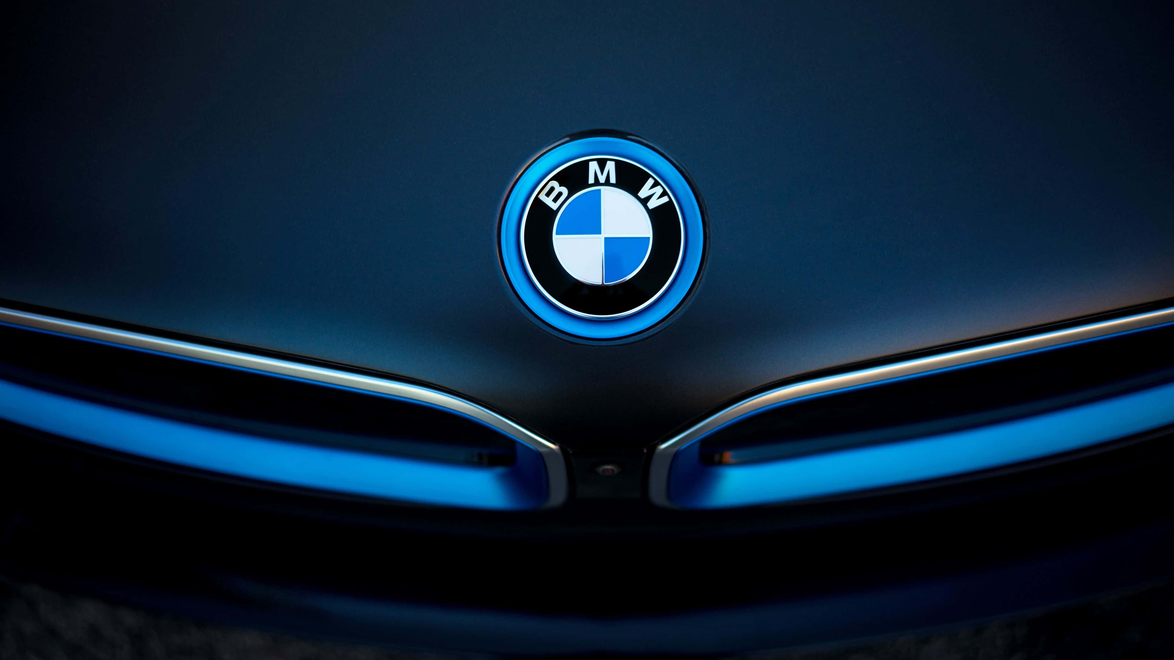 BMW 動圖 桌布 壁紙 — 特寫鏡頭：BMW 標誌在戲劇性燈光下於時尚深色車頭蓋上發出藍光。