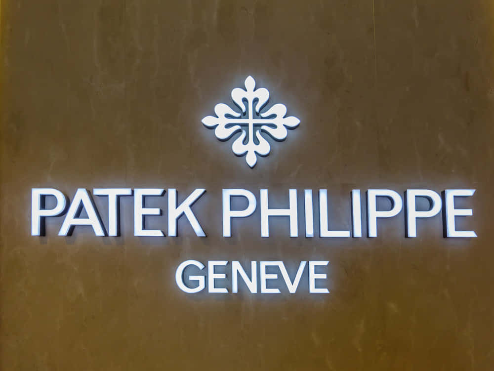 品牌 桌布 壁紙 — 特寫鏡頭：Patek Philippe Geneve 標誌，白色發光字體和標誌，位於紋理青銅牆上。