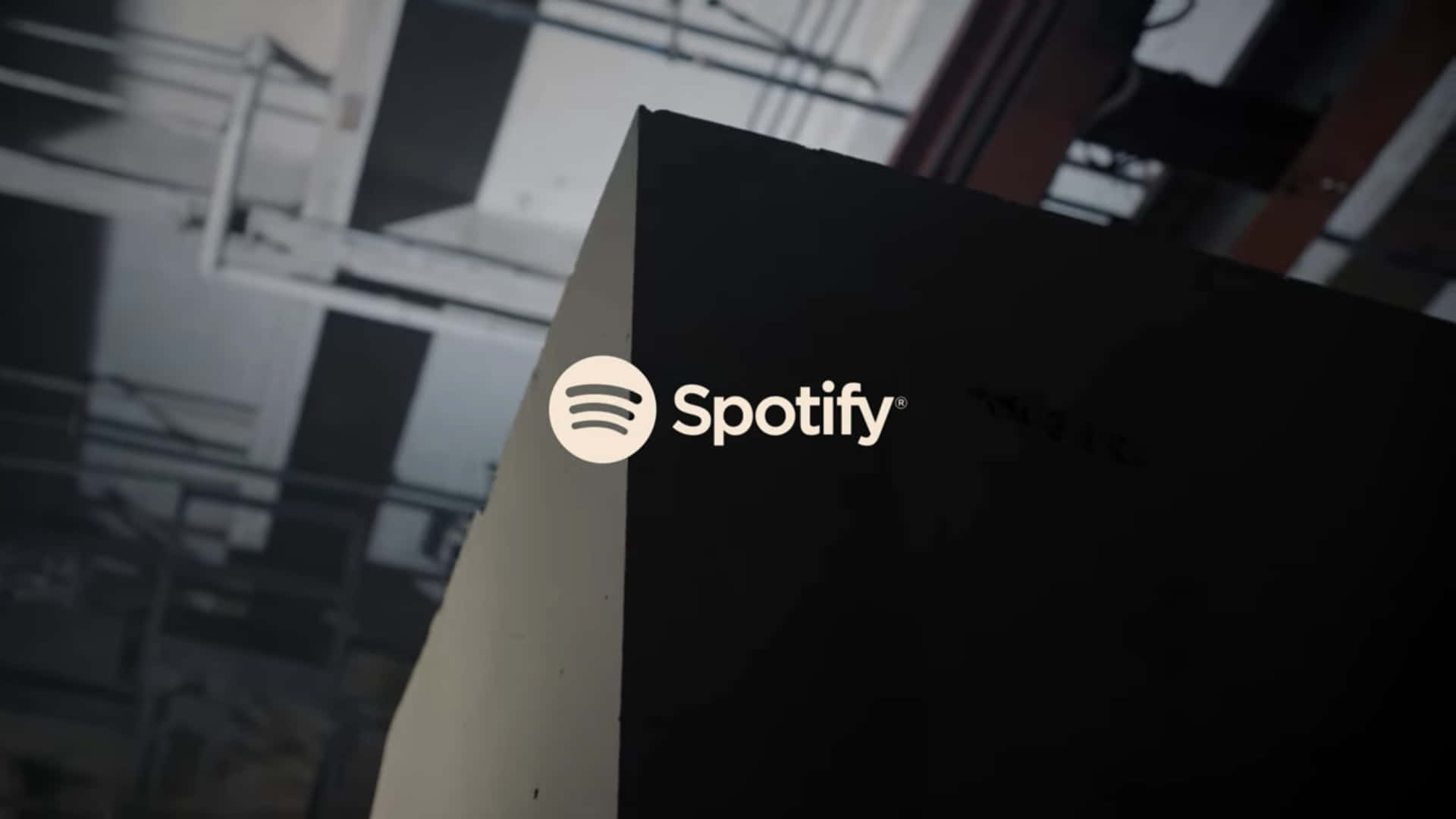 Spotify 桌布 壁紙 — 特寫鏡頭：Spotify 標誌在黑色表面上發出白色光芒，背景是模糊的工業環境。