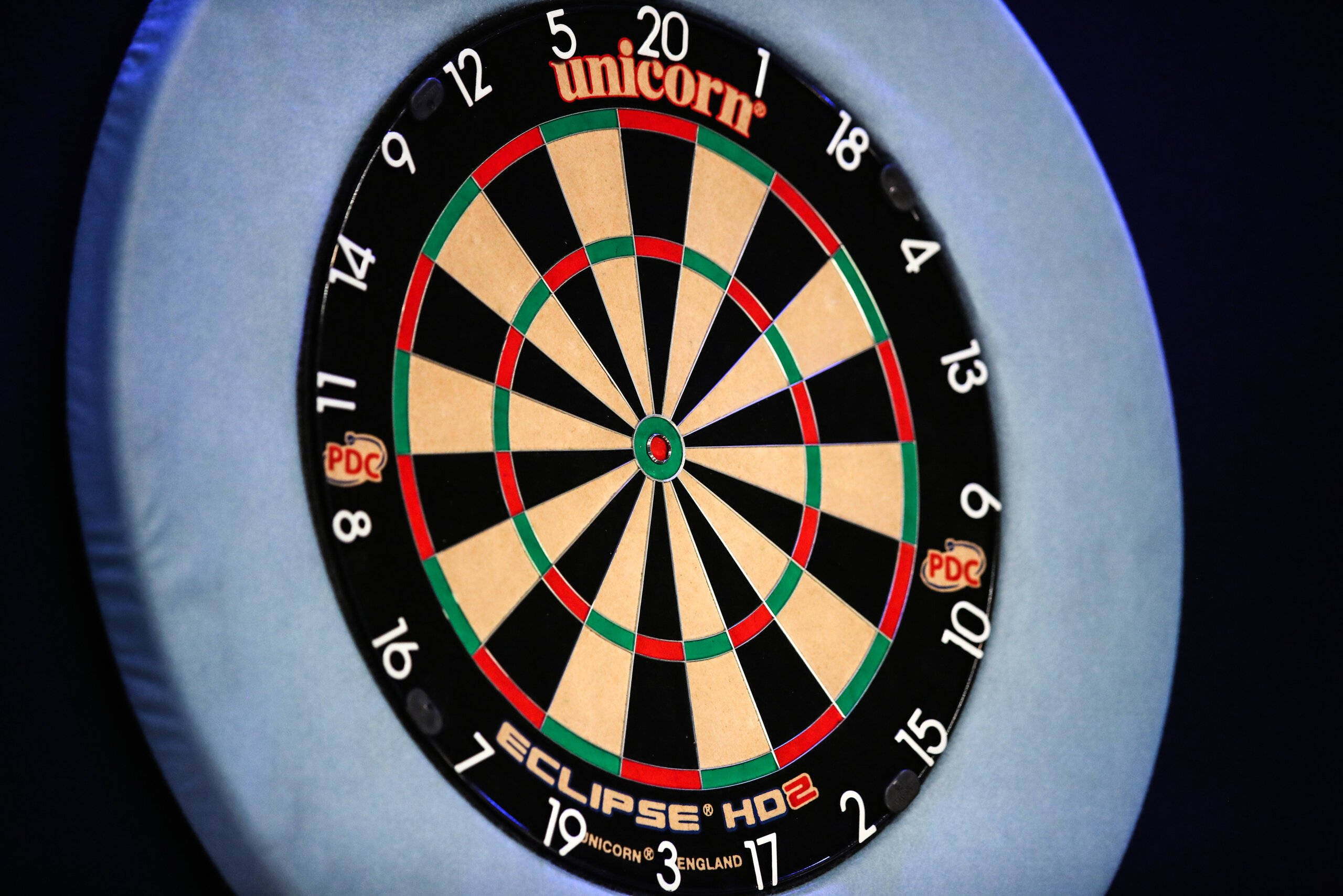 darts 桌布 壁紙 — 特寫鏡頭：Unicorn Eclipse HD2 飛鏢靶，在聚焦燈光下呈現紅、綠、黑三色區域。