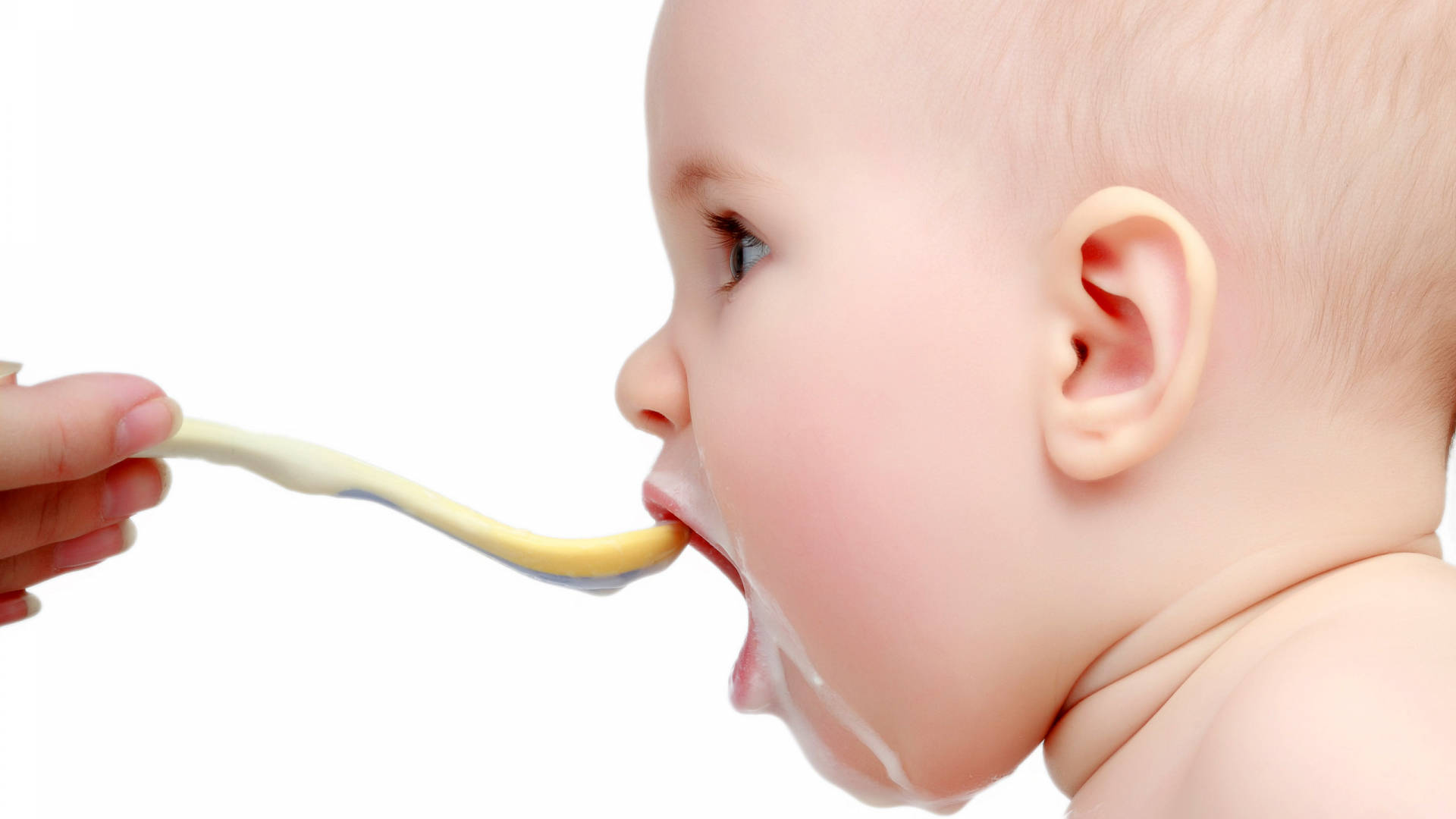 Funny Baby 桌布 壁紙 — 特寫鏡頭，一個嬰兒正在急切地從成人手持的湯匙中吃黃色泥狀食物，背景為白色。