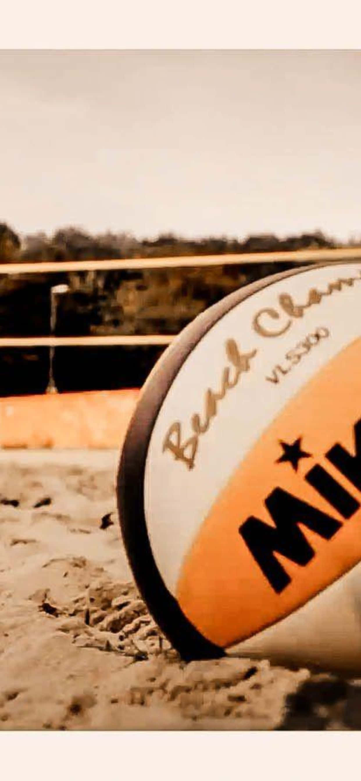 iPhone Xs Max Volleyball 桌布 壁紙 — 特寫鏡頭，一個有品牌的沙灘排球擱在沙上，背景有網和樹木，呈現柔和焦點。
