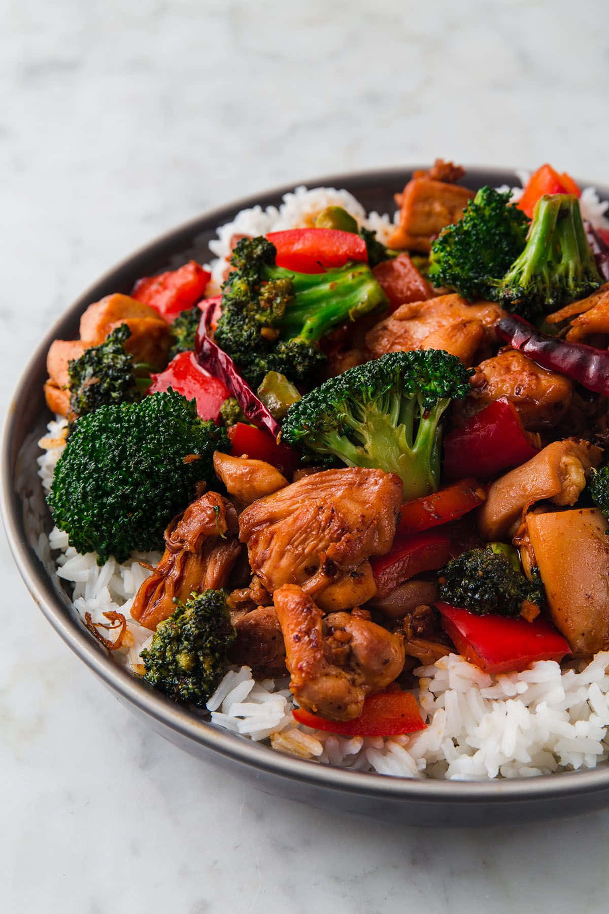Chinese Food 桌布 壁紙 — 特寫鏡頭：一個深色碗中盛載著放在白飯上的美味雞肉西蘭花炒菜，置於大理石表面上。