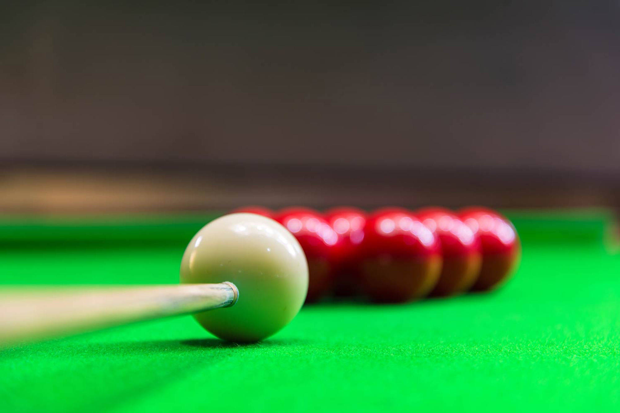 Snooker 桌布 壁紙 — 特寫鏡頭，一個白球觸碰著撞球桿，背景中有紅色球模糊在綠色絨布桌上。