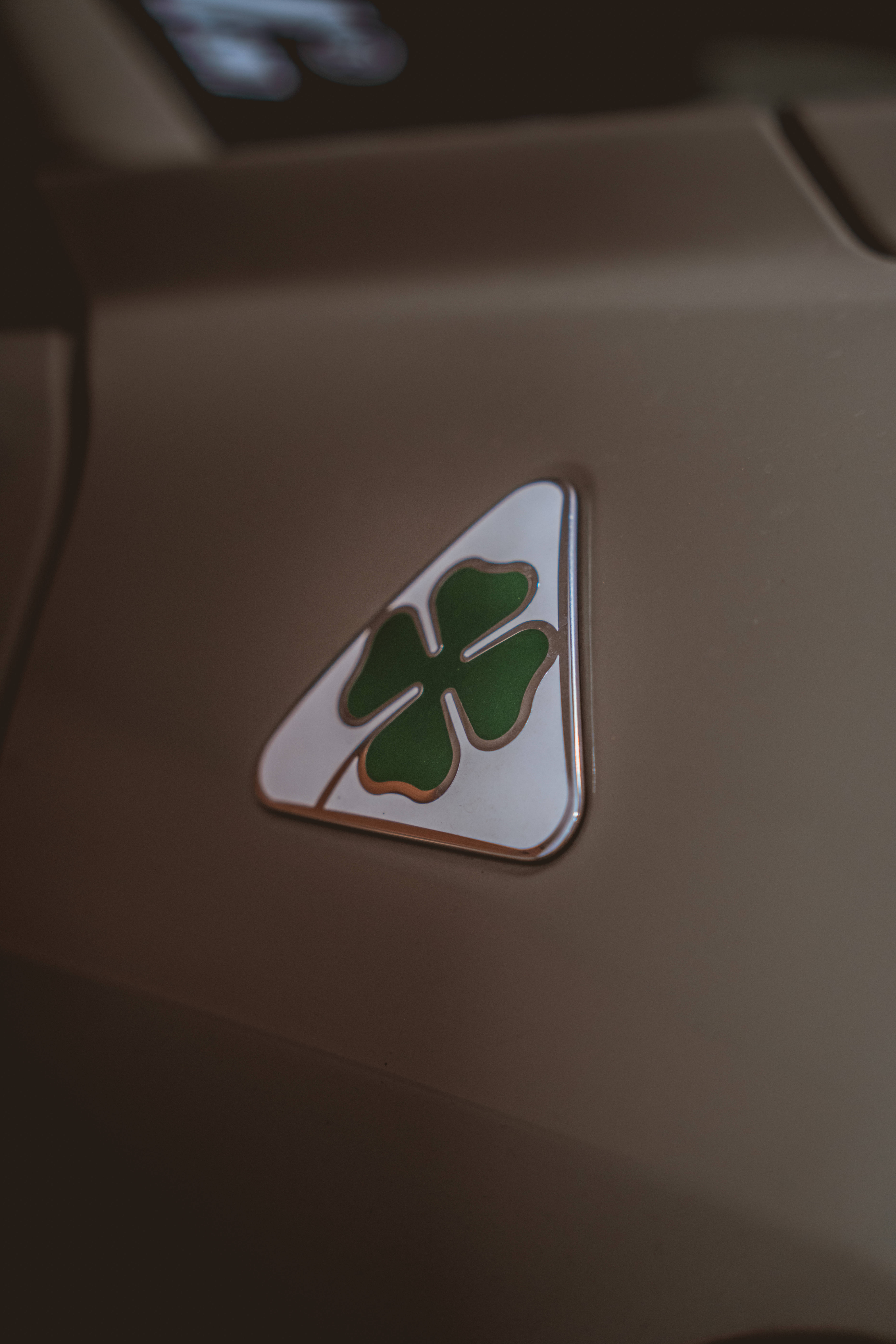 Alfa Romeo 桌布 壁紙 — 特寫鏡頭：一個綠色四葉草標誌位於白色三角形徽章上，安裝在米色汽車內飾板上。
