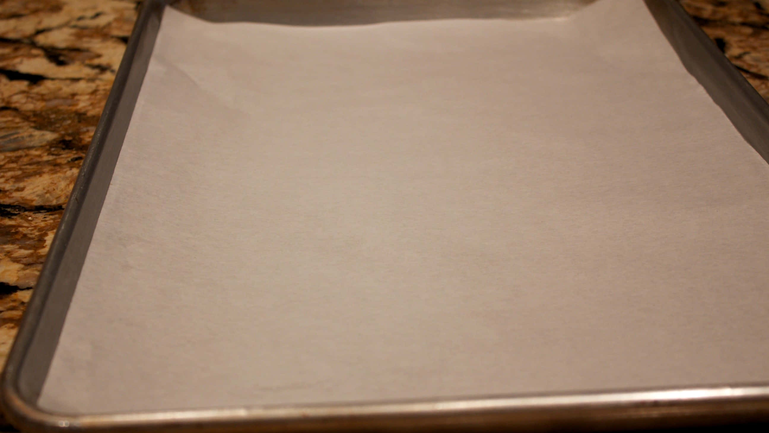 Parchment 桌布 壁紙 — 特寫鏡頭：一個金屬烤盤，上面鋪著白色烘焙紙，放在有斑點的檯面上。