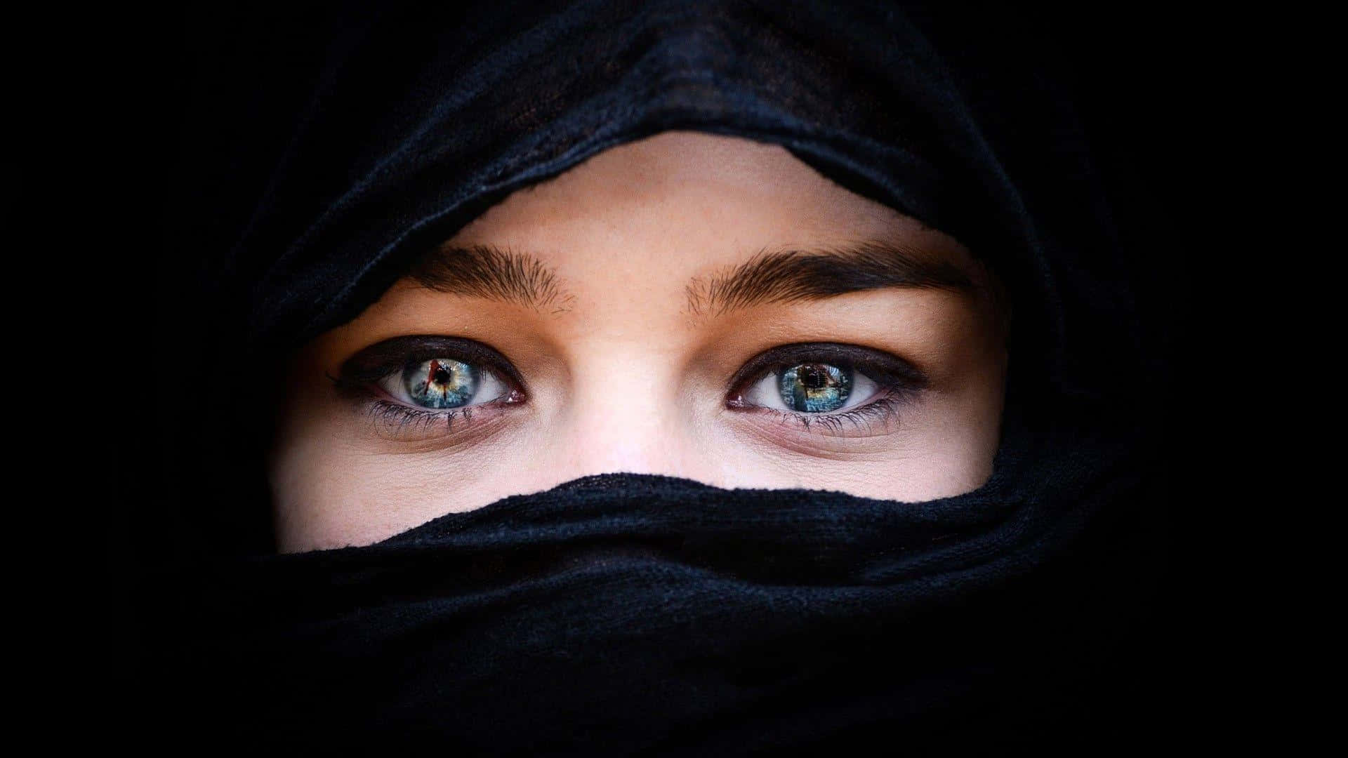 arabic 桌布 壁紙 — 特寫鏡頭：一名女性深邃的藍色眼睛從黑色面紗下窺視，背景為深色。