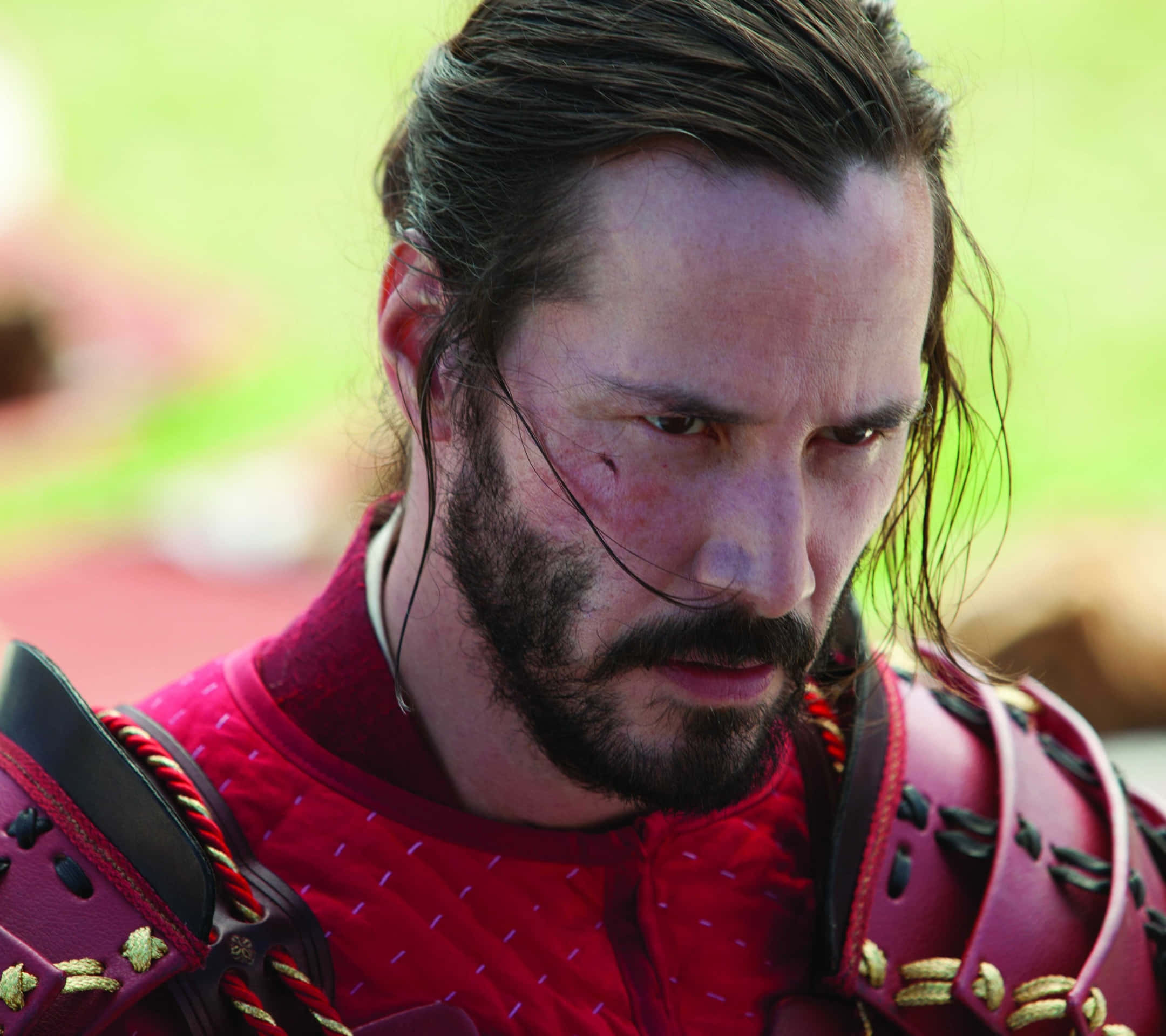 47 Ronin 桌布 壁紙 — 特寫鏡頭：一名武士戰士，滿臉鮮血，眼神凌厲，身穿紅色盔甲，背景是模糊的綠色。
