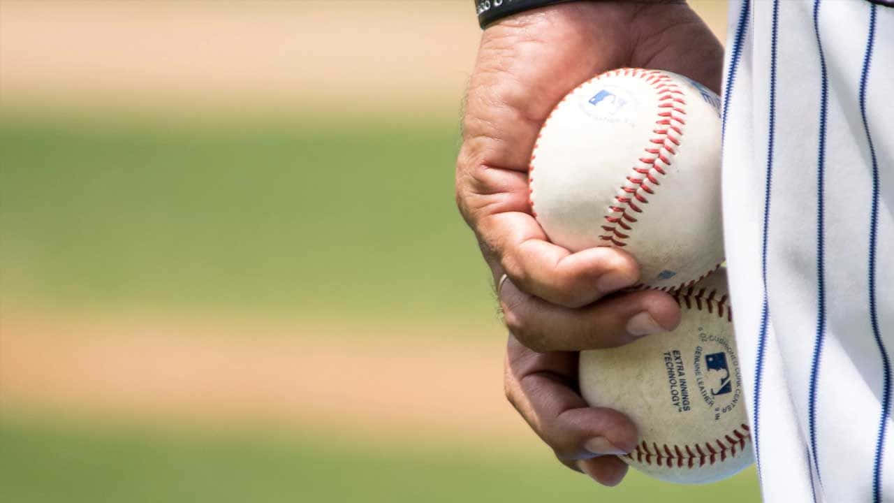 sport 桌布 壁紙 — 特寫鏡頭，一名歷經風霜的棒球選手的手緊握兩個官方棒球，背景是模糊的綠色球場。