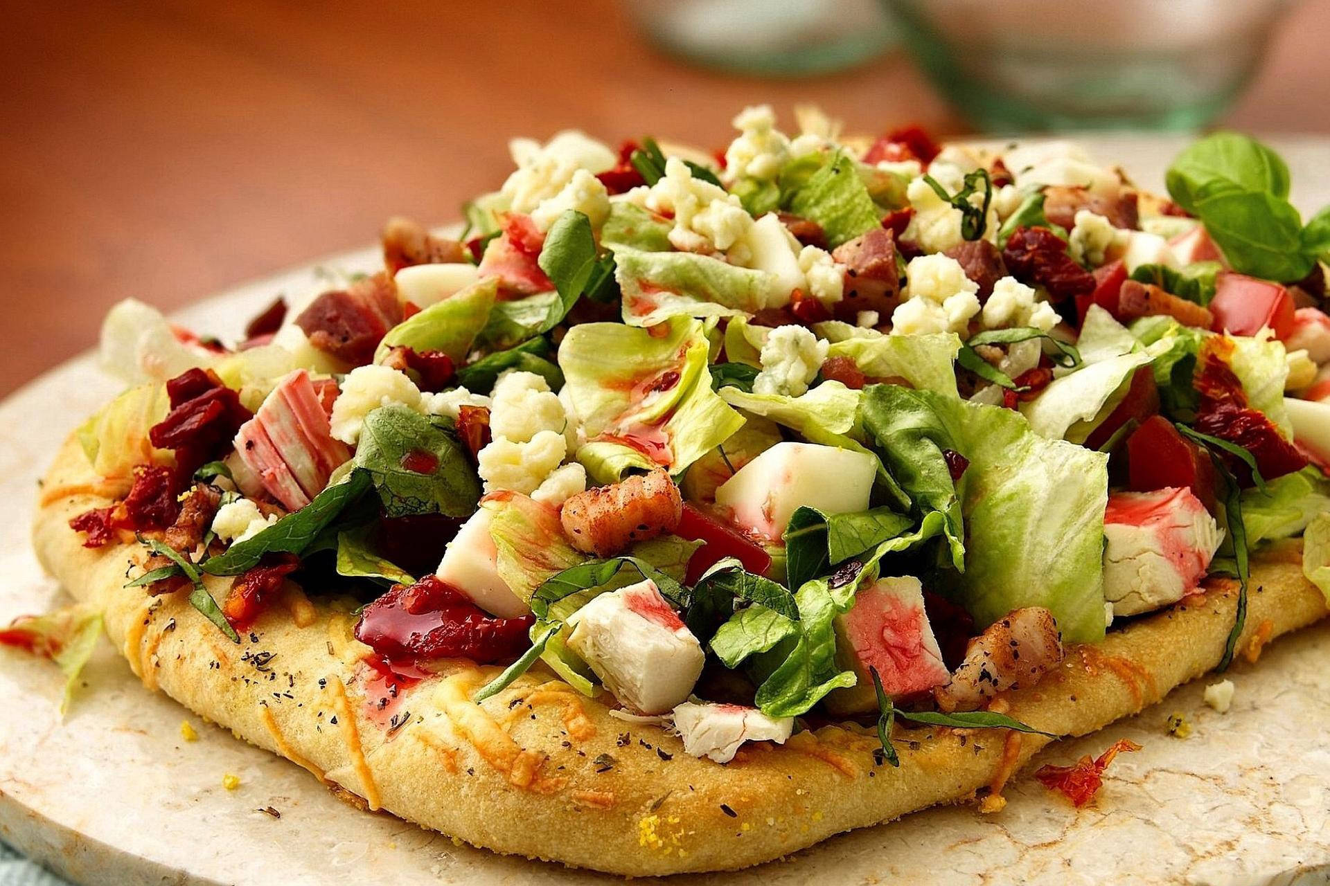 Pizza 桌布 壁紙 — 特寫鏡頭：一塊扁麵包披薩，上面鋪上新鮮生菜、碎菲達起司、培根和曬乾番茄，放在大理石板上。