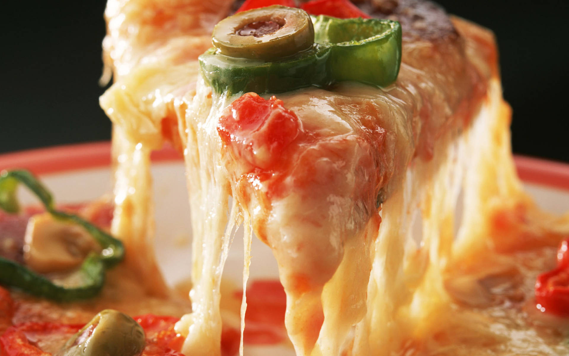 Pizza 桌布 壁紙 — 特寫鏡頭，一塊起司披薩片，上面有橄欖和青椒，融化的起司滴落，背景深色。