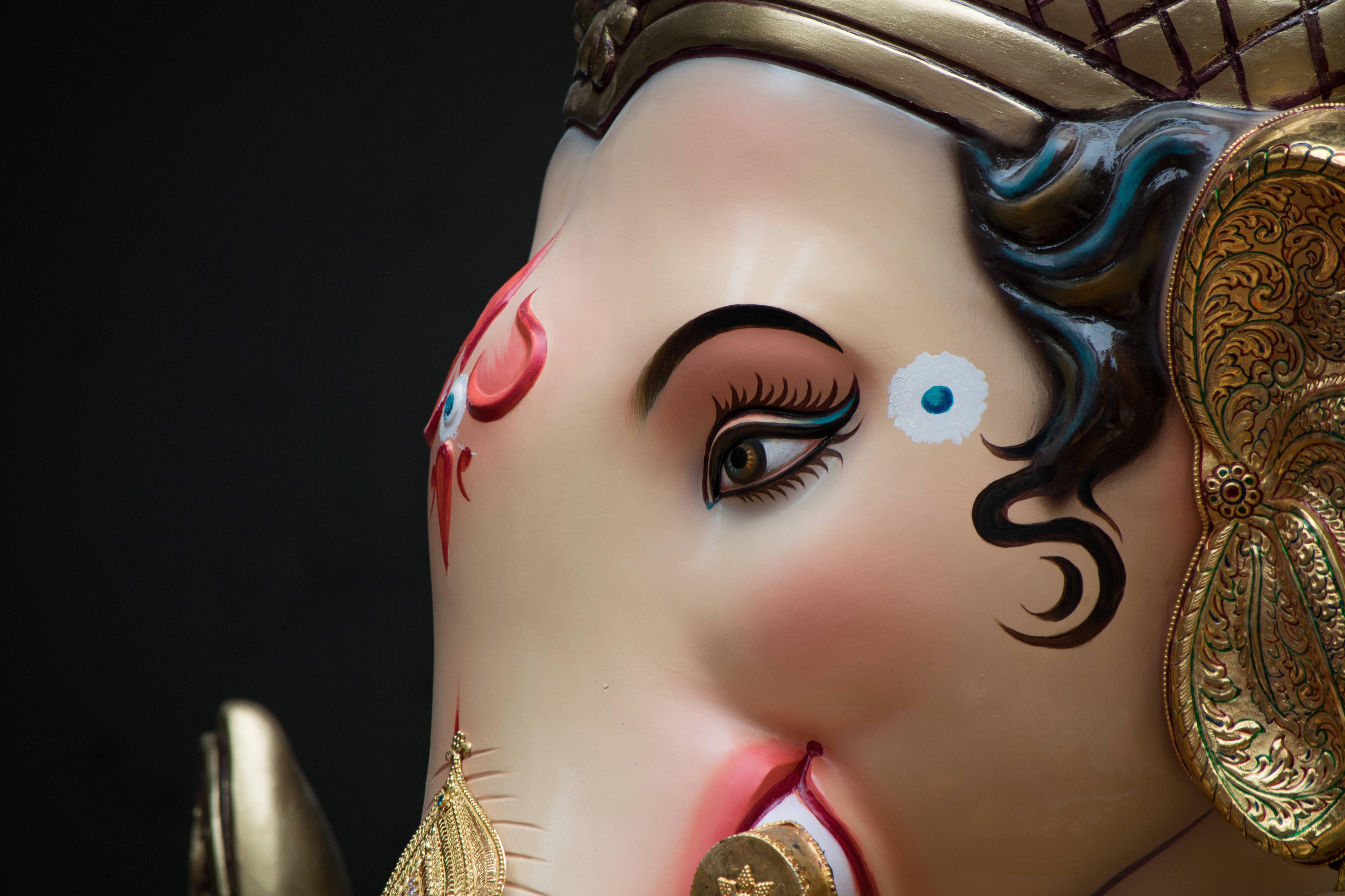 ganpati HD 桌布 壁紙 — 特寫鏡頭：一尊色彩鮮豔的象頭神像，戴著金冠和華麗珠寶，背景為黑色。