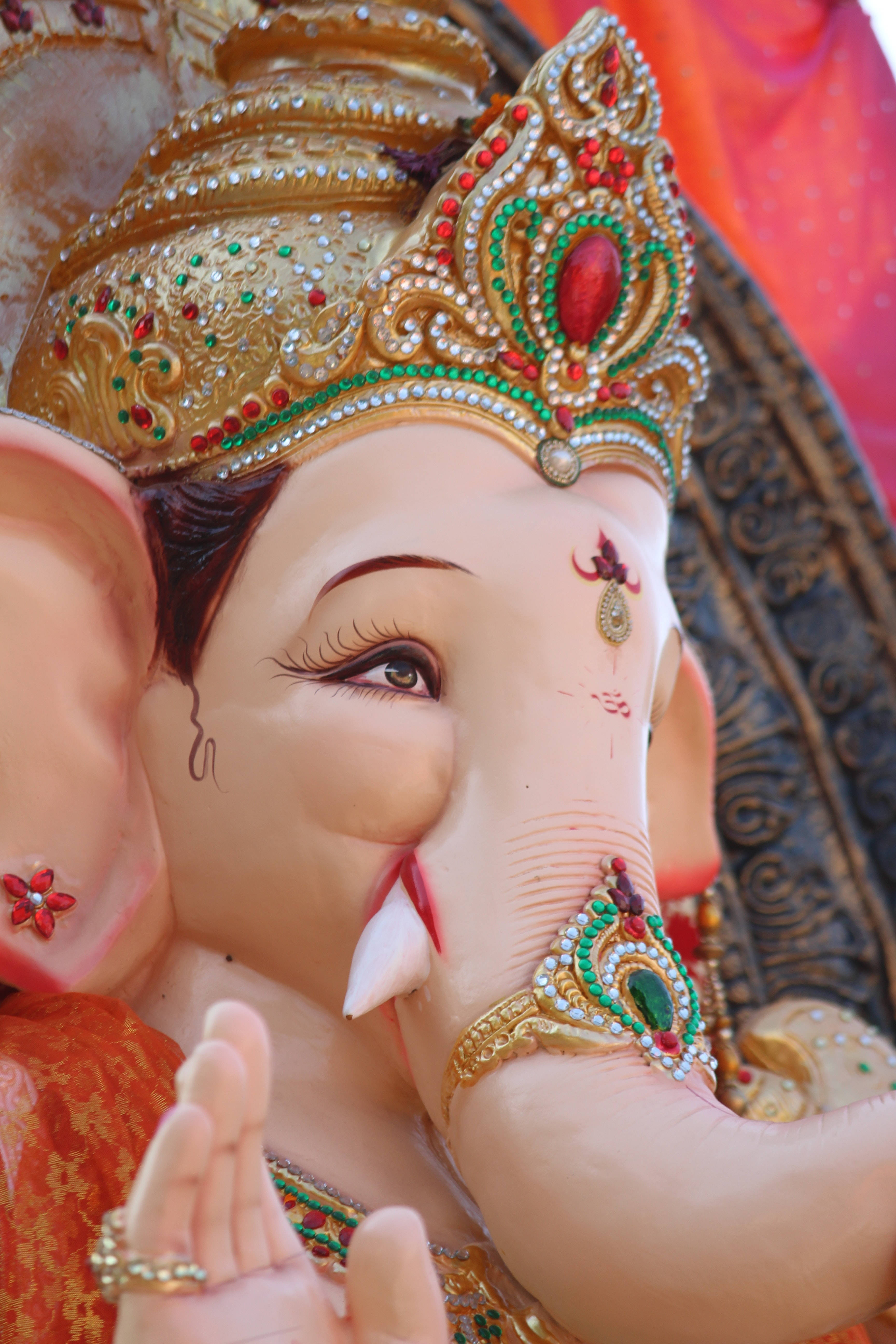 ganesh 4K 桌布 壁紙 — 特寫鏡頭：一尊裝飾華麗的象頭神像，帶有金色皇冠珠寶和彩繪細節，背景為鮮紅色布料。