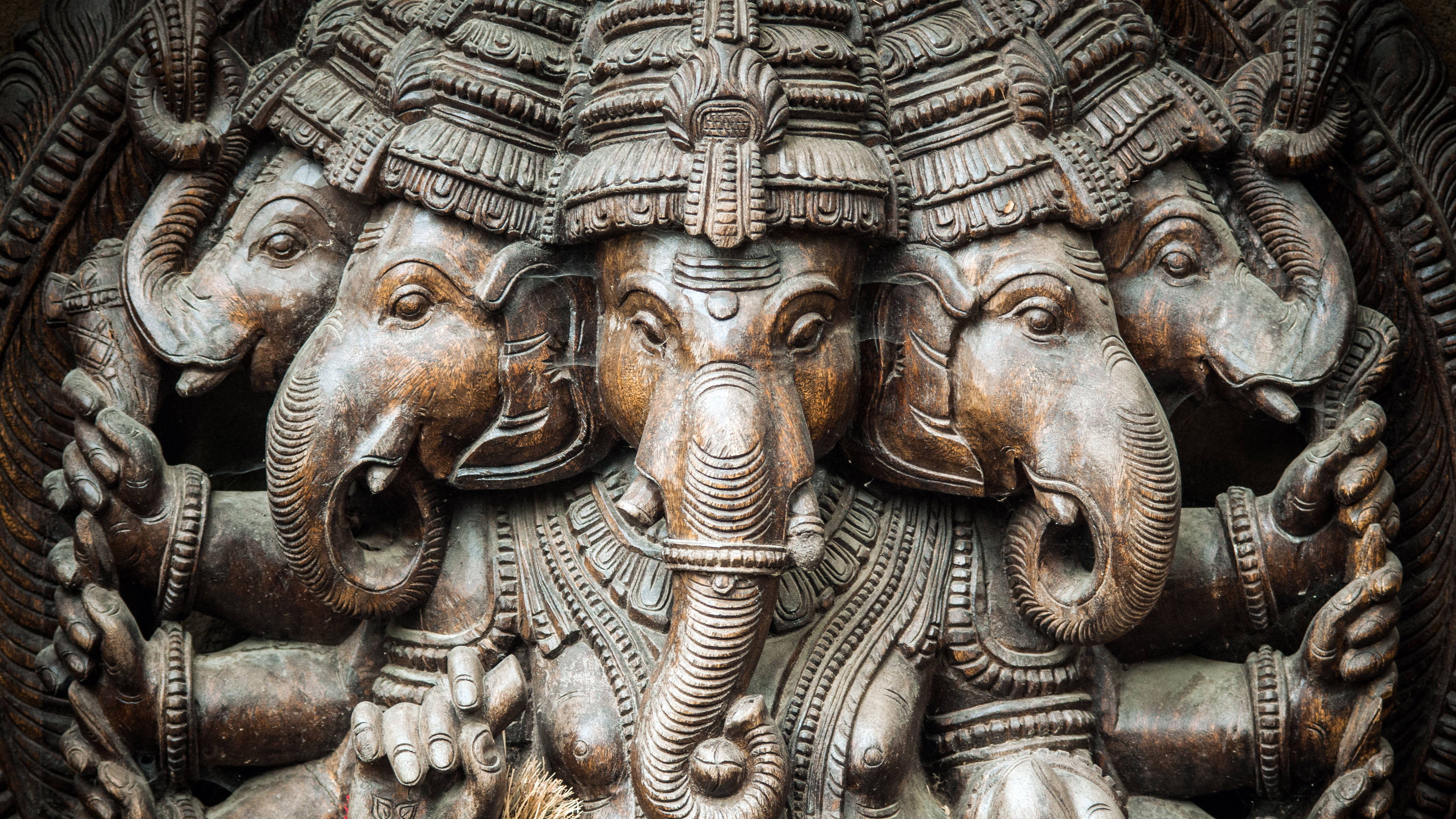 Ganesh 桌布 壁紙 — 特寫鏡頭：一尊雕刻精緻的多頭象神木雕，飾有華麗頭飾和珠寶。