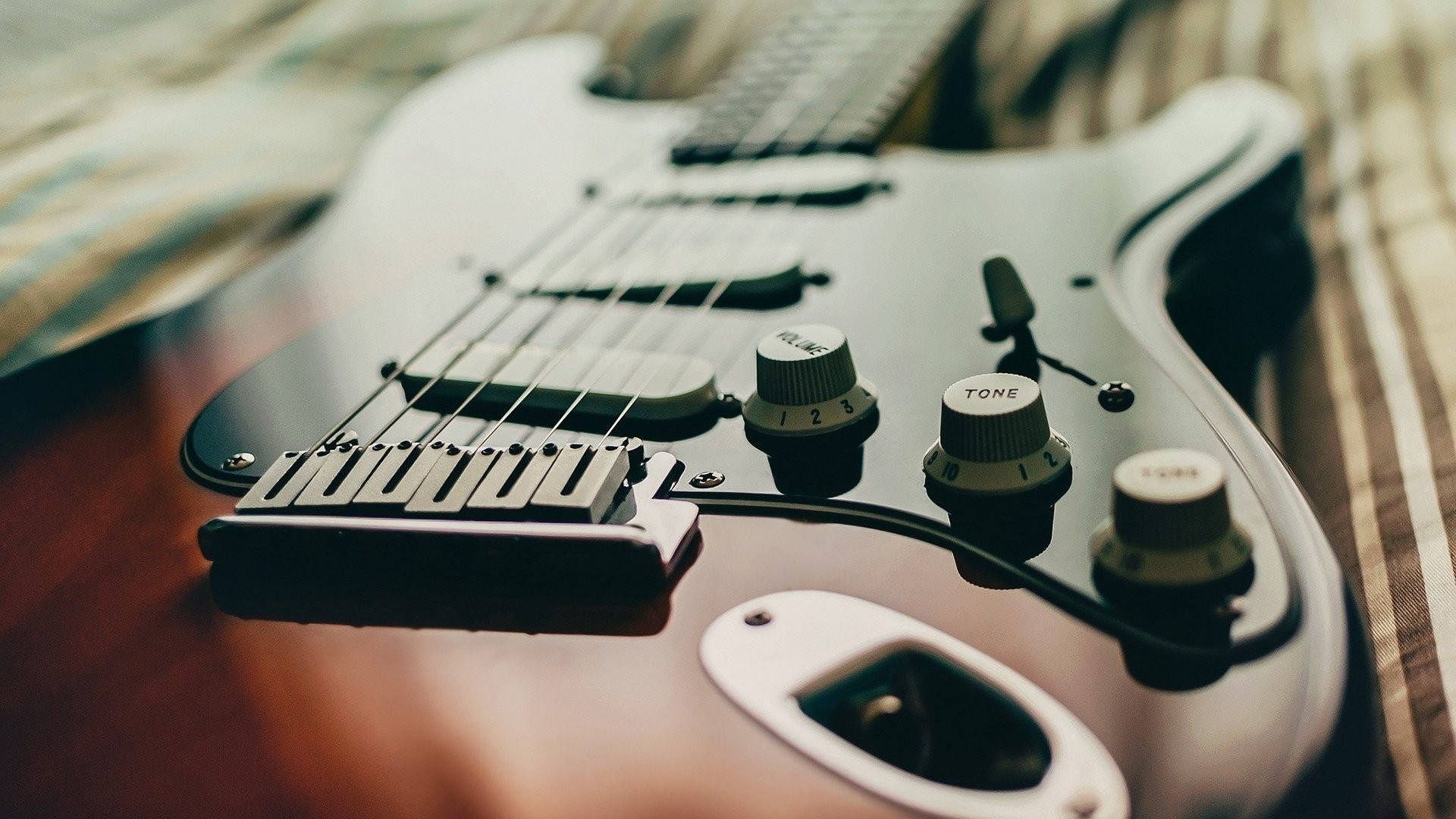 Musical Instrument 桌布 壁紙 — 特寫鏡頭：一把時尚的銀色電吉他放在條紋布料上，營造溫暖的淺景深效果。