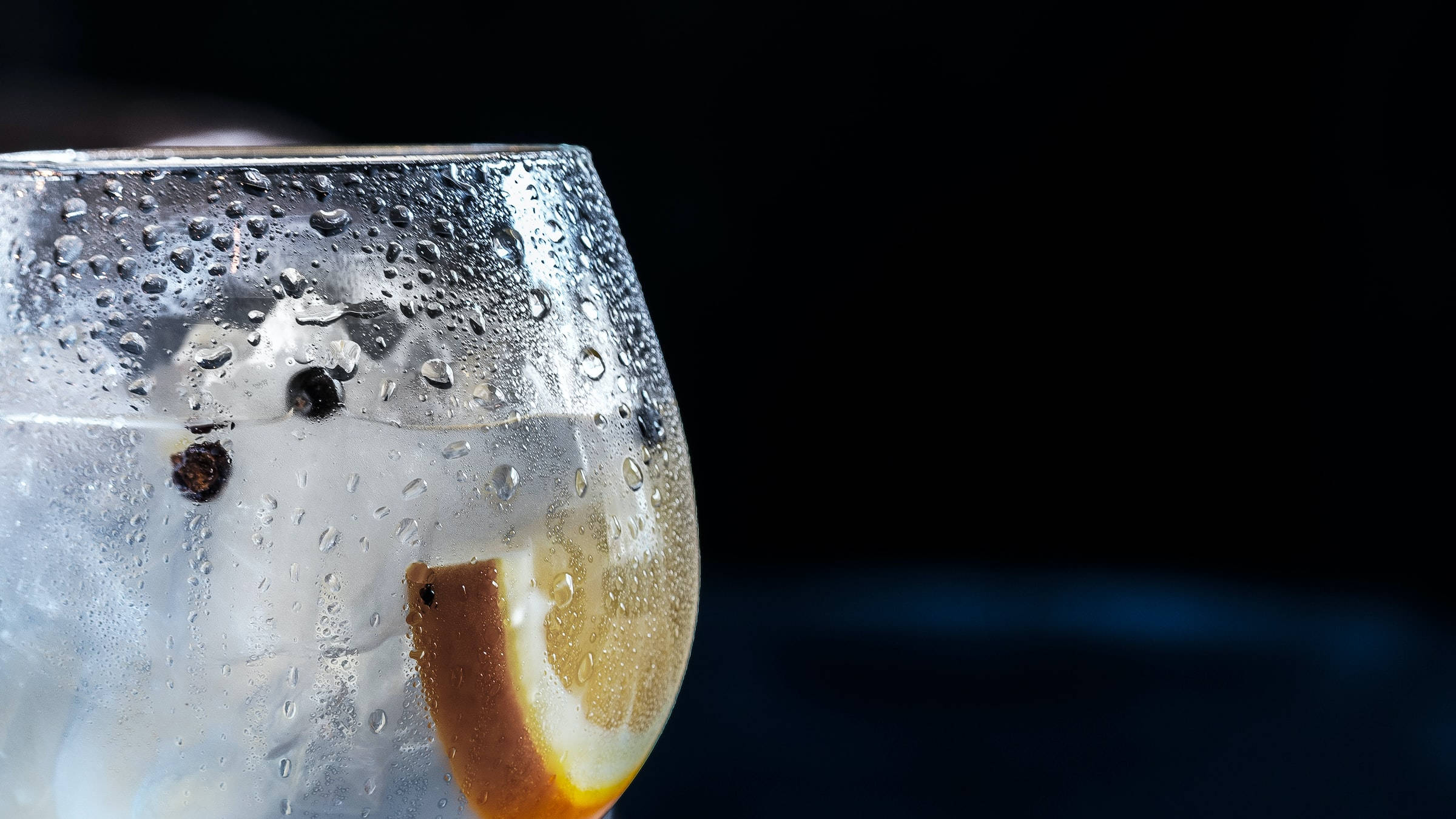 alcohol 桌布 壁紙 — 特寫鏡頭：一杯冰凍琴酒湯力水，杯身凝結水珠，配上檸檬片和黑胡椒粒，背景深色。
