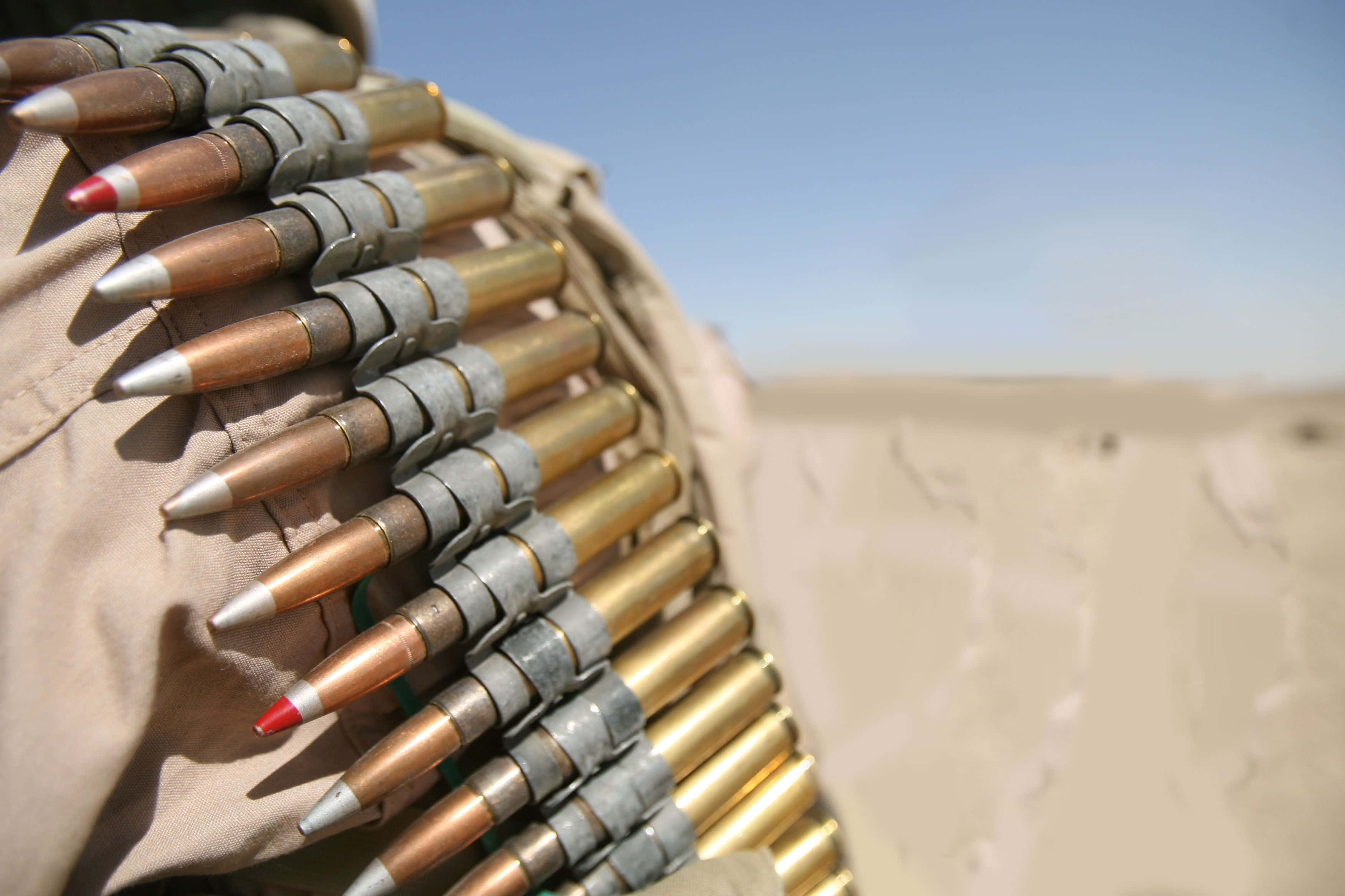 bullet 桌布 壁紙 — 特寫鏡頭：一條裝有黃銅彈藥的淺褐色軍用腰帶，背景是模糊的沙漠，在明亮的日光下。