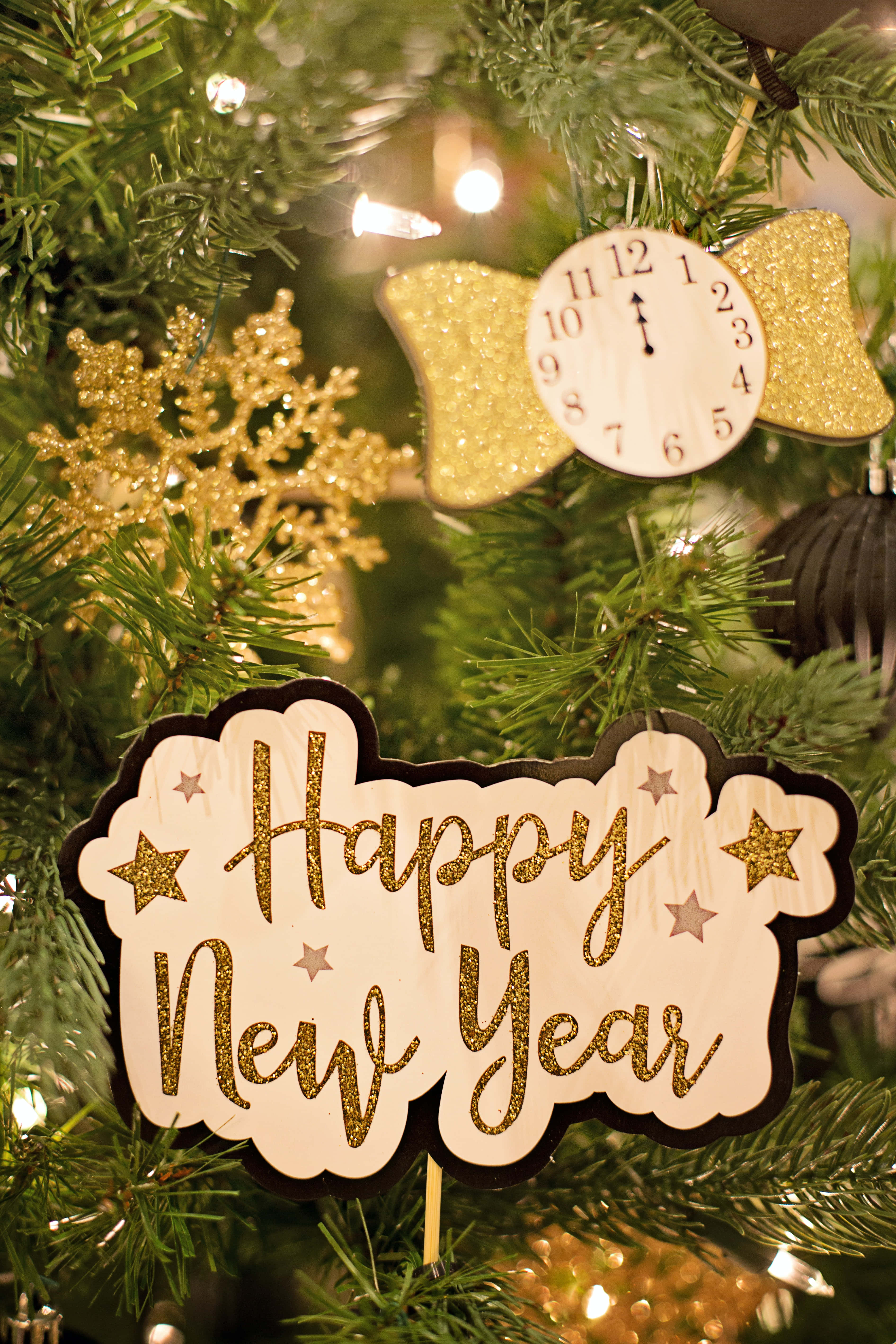 New Year 桌布 壁紙 — 特寫鏡頭：一棵聖誕樹，飾有閃爍的「Happy New Year」標牌、時鐘和金色裝飾品，在溫暖燈光下。