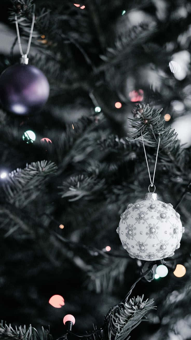 Aesthetic Christmas Tree 桌布 壁紙 — 特寫鏡頭：一棵裝飾好的聖誕樹，帶有白色華麗裝飾球和紫色飾物，背景是模糊的節日燈光。