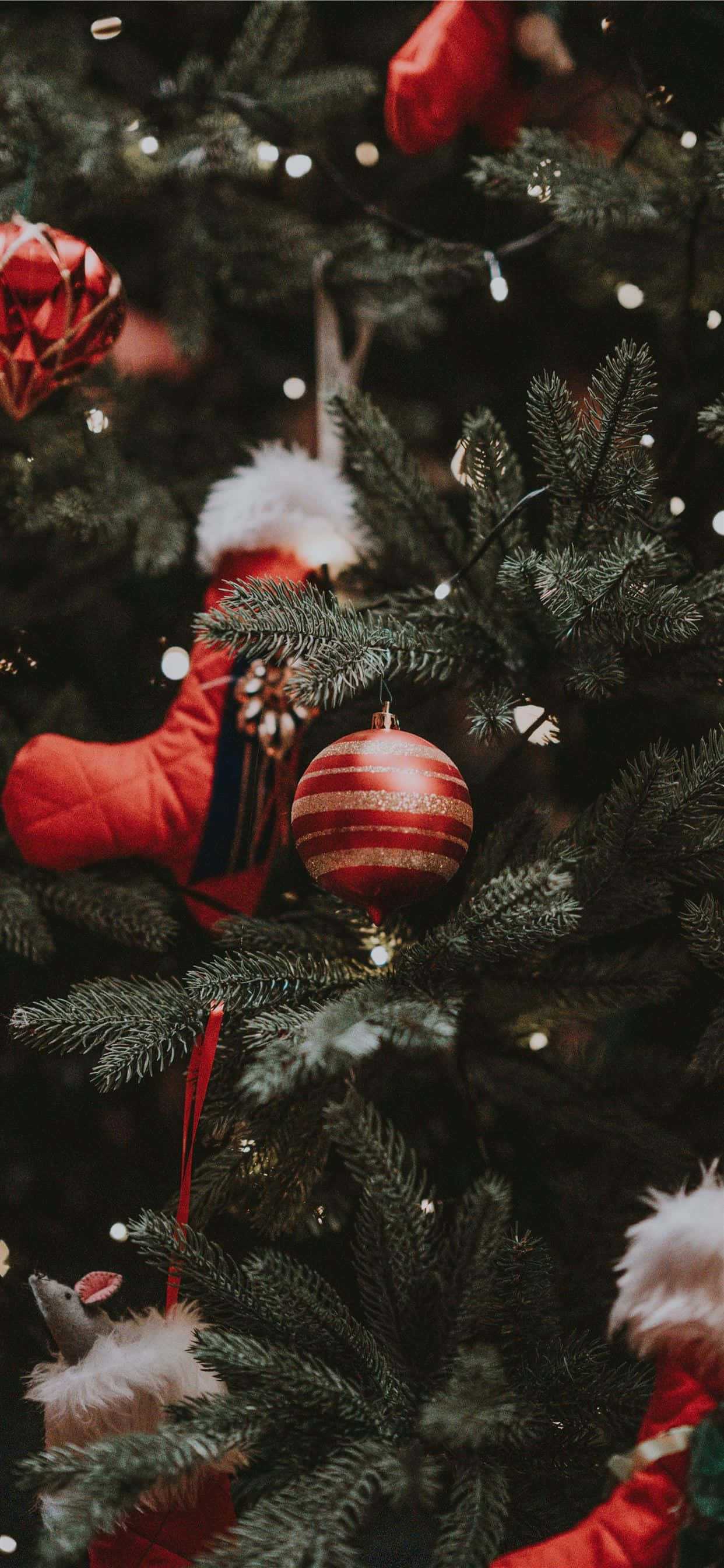 Christmas Tree iPhone 桌布 壁紙 — 特寫鏡頭：一棵裝飾華麗的聖誕樹，掛滿紅色條紋飾物和毛絨紅襪，在溫暖的仙女燈下閃爍光芒。