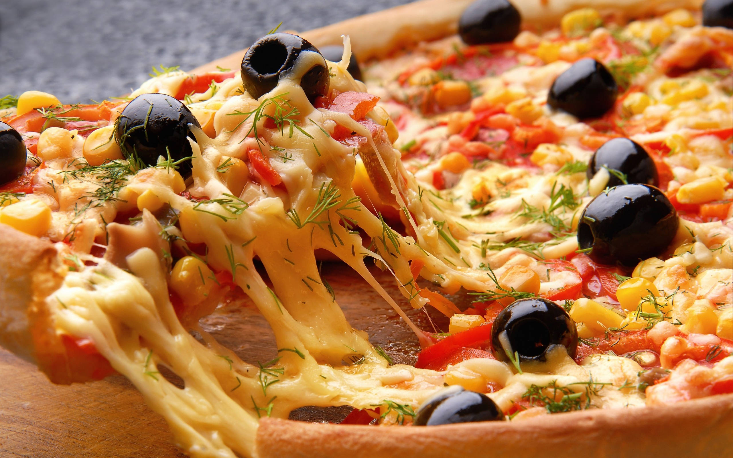 Pizza 桌布 壁紙 — 特寫鏡頭，一片起司披薩被提起，露出拉絲的起司和橄欖、玉米、香草等配料。