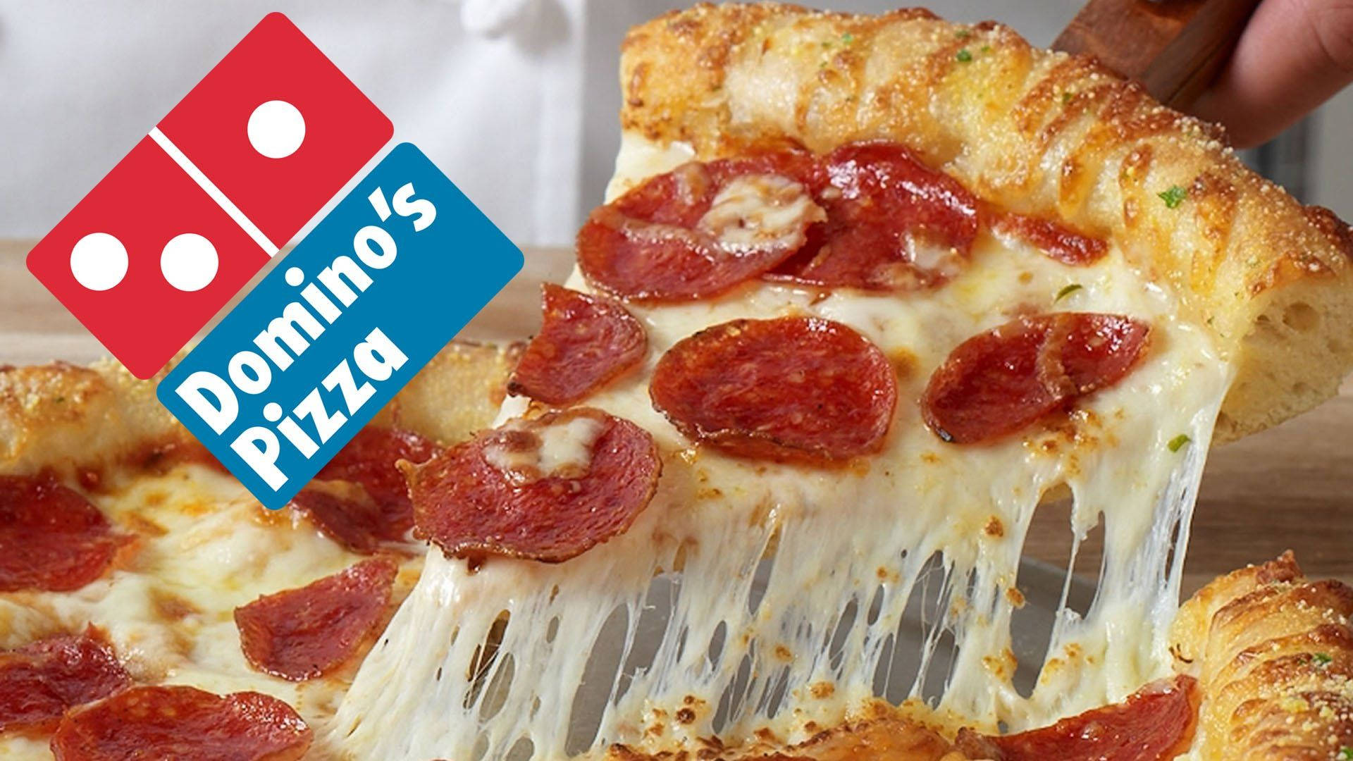 Dominos Pizza 桌布 壁紙 — 特寫鏡頭：一片起司辣肉腸披薩被拿起，帶有黏稠拉絲的起司，並疊加Domino's Pizza標誌。