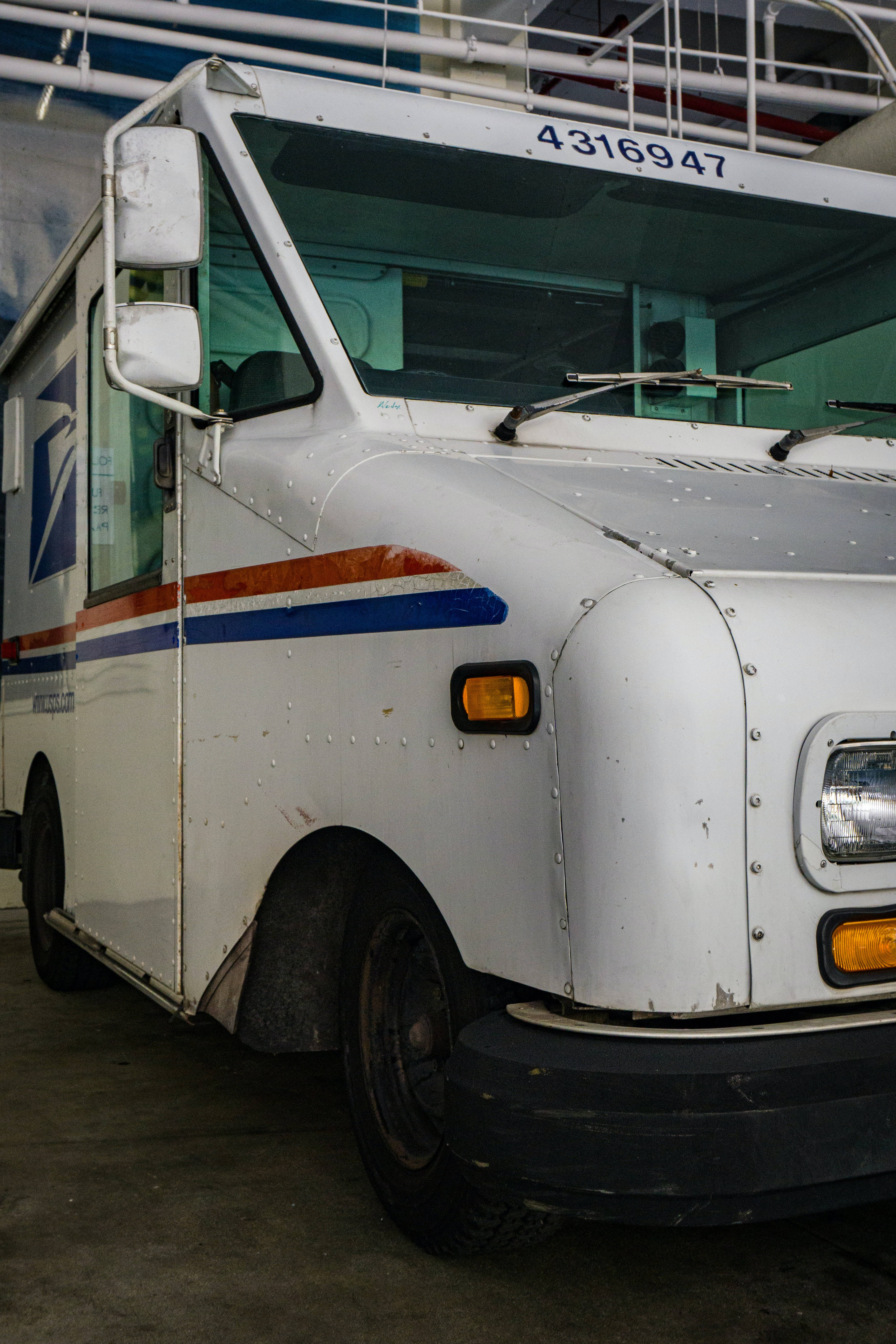 Trucks 桌布 壁紙 — 特寫鏡頭：一輛風化的白色USPS郵政貨車停放在室內，車頭有明顯的磨損痕跡。
