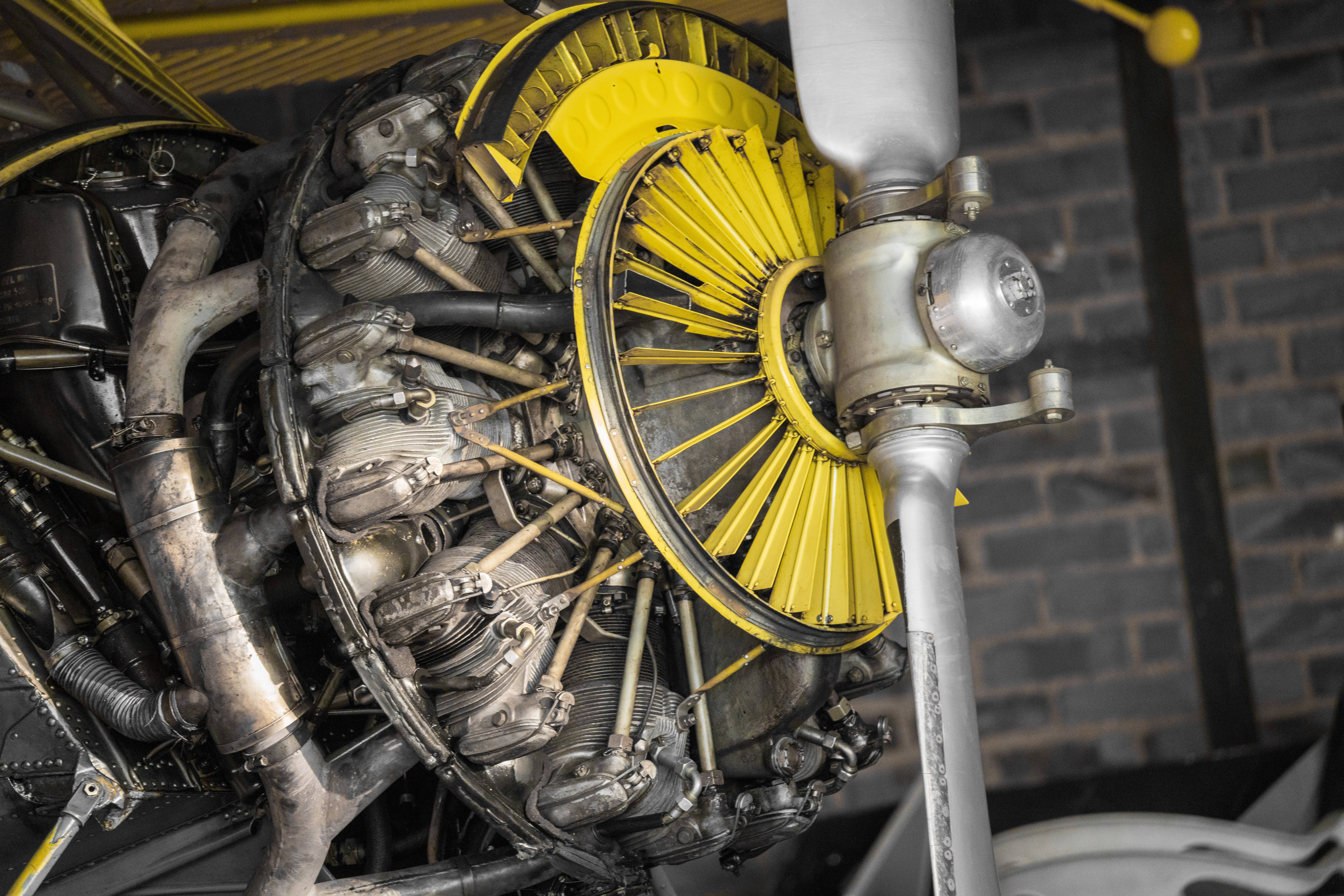 Engine 桌布 壁紙 — 特寫鏡頭：一部復古星形飛機引擎，帶有亮黃色螺旋槳整流罩，背景是深色磚牆。