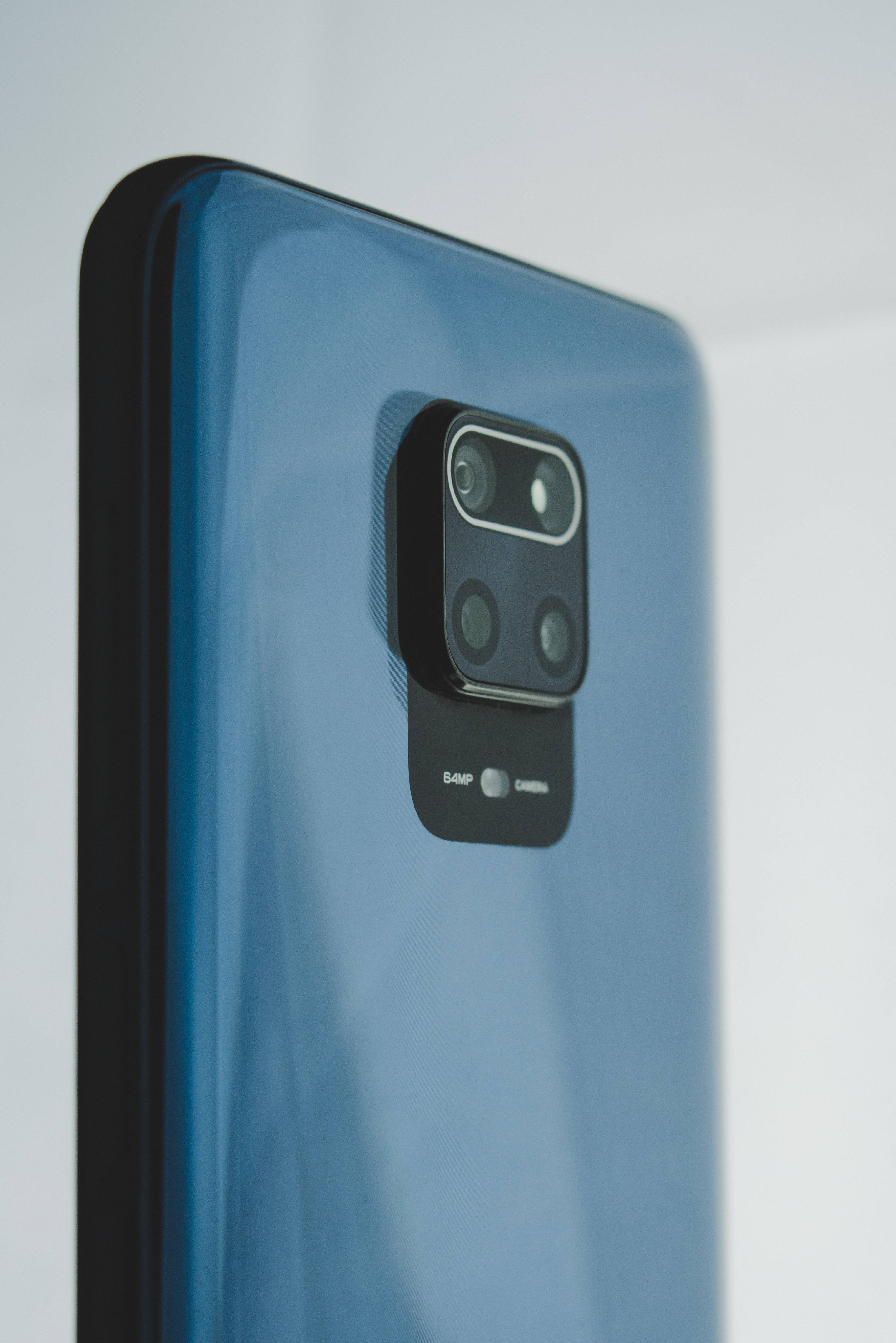 Xiaomi 桌布 壁紙 — 特寫鏡頭：一部時尚的藍色智慧型手機，帶有黑色四鏡頭模組，置於柔和的白色背景上。