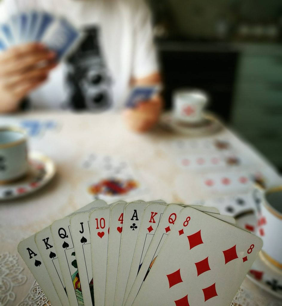 bridge 桌布 壁紙 — 特寫鏡頭：一隻手在蕾絲桌布上展開撲克牌，背景有模糊的茶杯和一部復古相機。