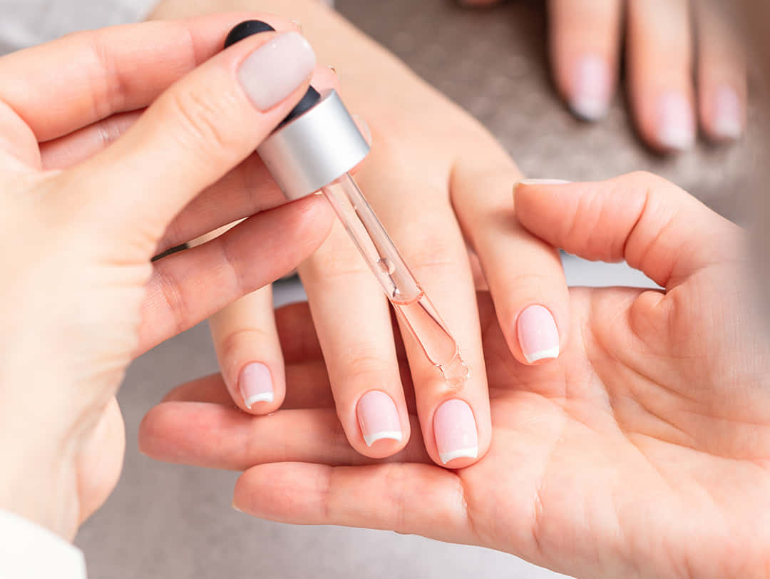 Manicure 桌布 壁紙 — 特寫鏡頭，一隻手用銀色滴管將透明精華液滴到另一隻塗有柔和粉紅色美甲的手上。