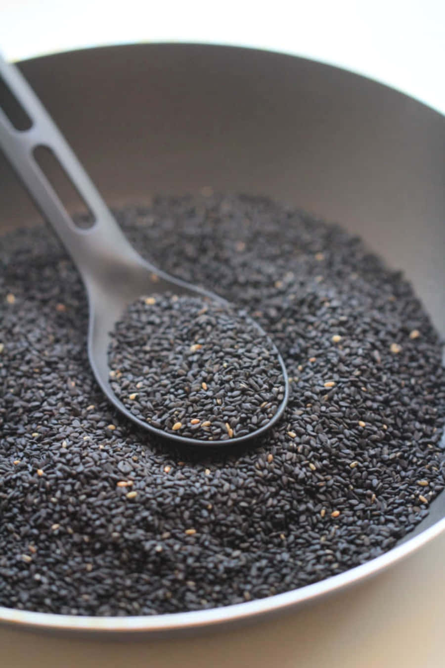 Black Sesame 桌布 壁紙 — 特寫鏡頭，一隻黑色湯匙盛著黑芝麻，置於裝滿相同芝麻的碗上方。