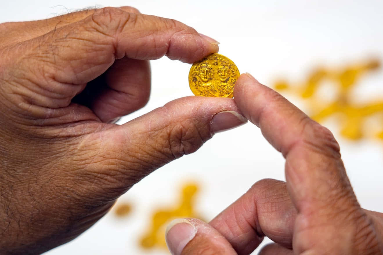 Coin 桌布 壁紙 — 特寫鏡頭，一雙飽經風霜的手小心翼翼地拿著一枚精緻的小金幣，背景是模糊的白色。
