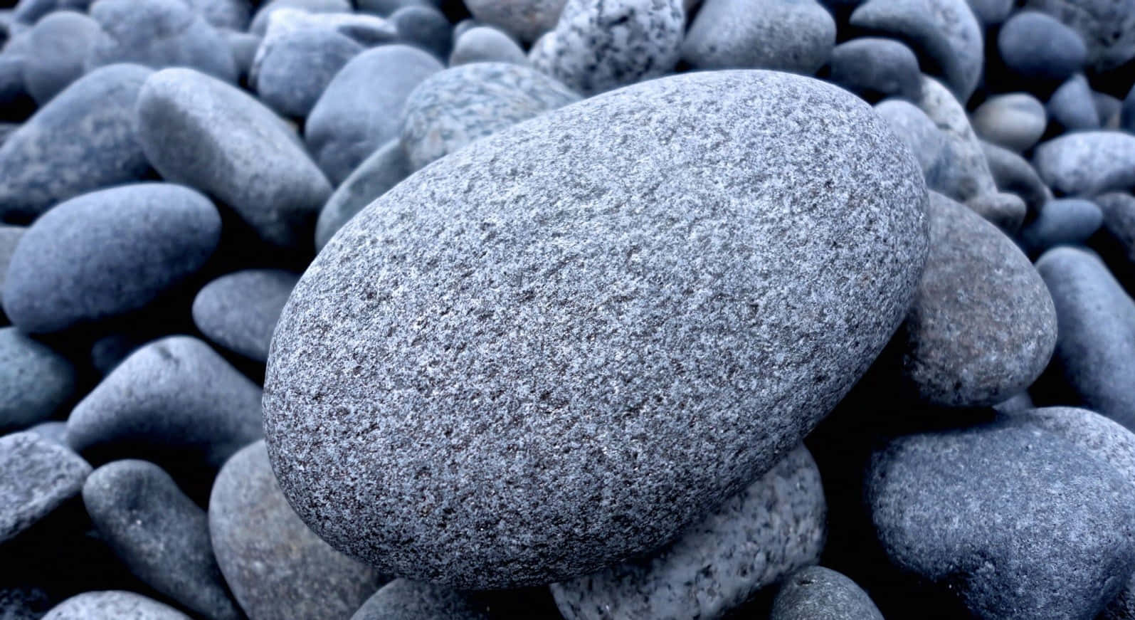 Stone 桌布 壁紙 — 特寫鏡頭：一顆光滑的灰色大卵石，周圍環繞著較小的圓形石頭，色調偏冷。