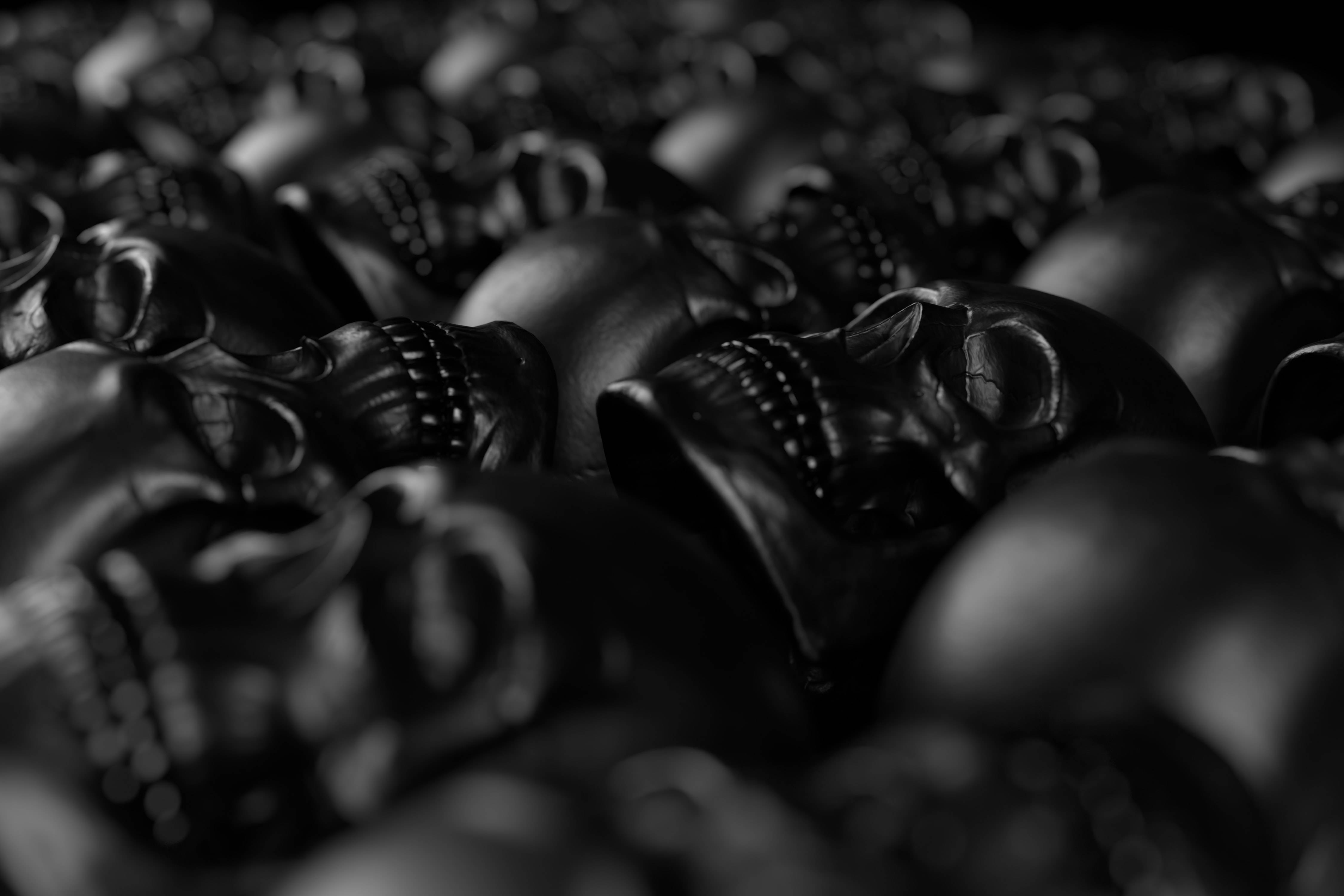 skulls 桌布 壁紙 — 特寫鏡頭，光澤黑色塑膠頭骨堆疊在一起，淺景深，戲劇性燈光。