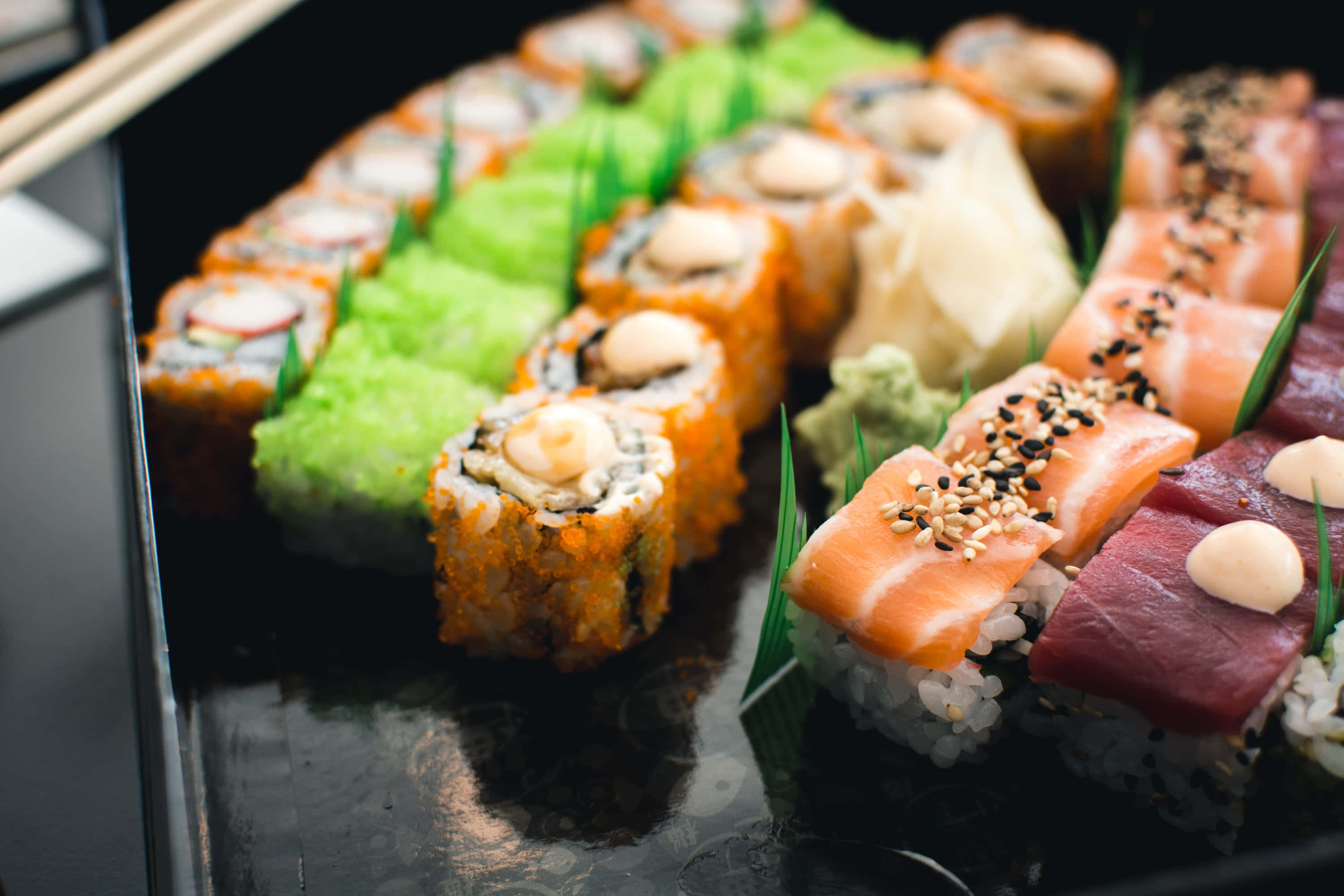 Sushi 桌布 壁紙 — 特寫鏡頭：各款壽司卷和生魚片整齊排列在黑盤上，搭配芥末和生薑。